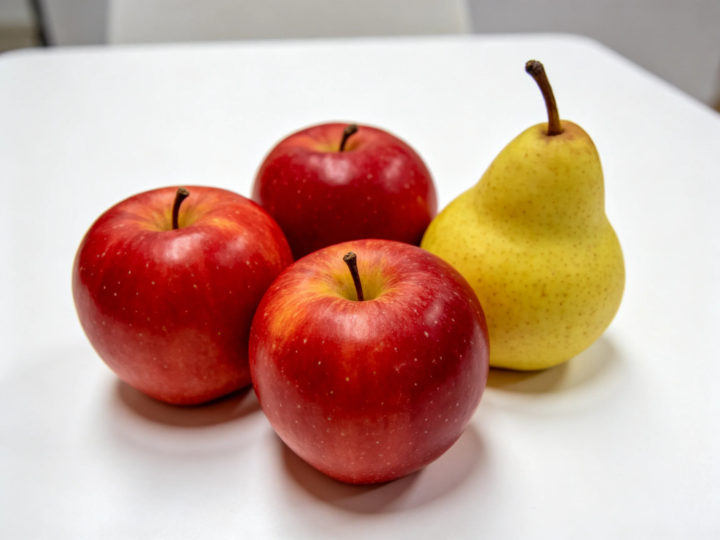 Three vibrant red apples and a golden-yellow pear arranged on a white surface