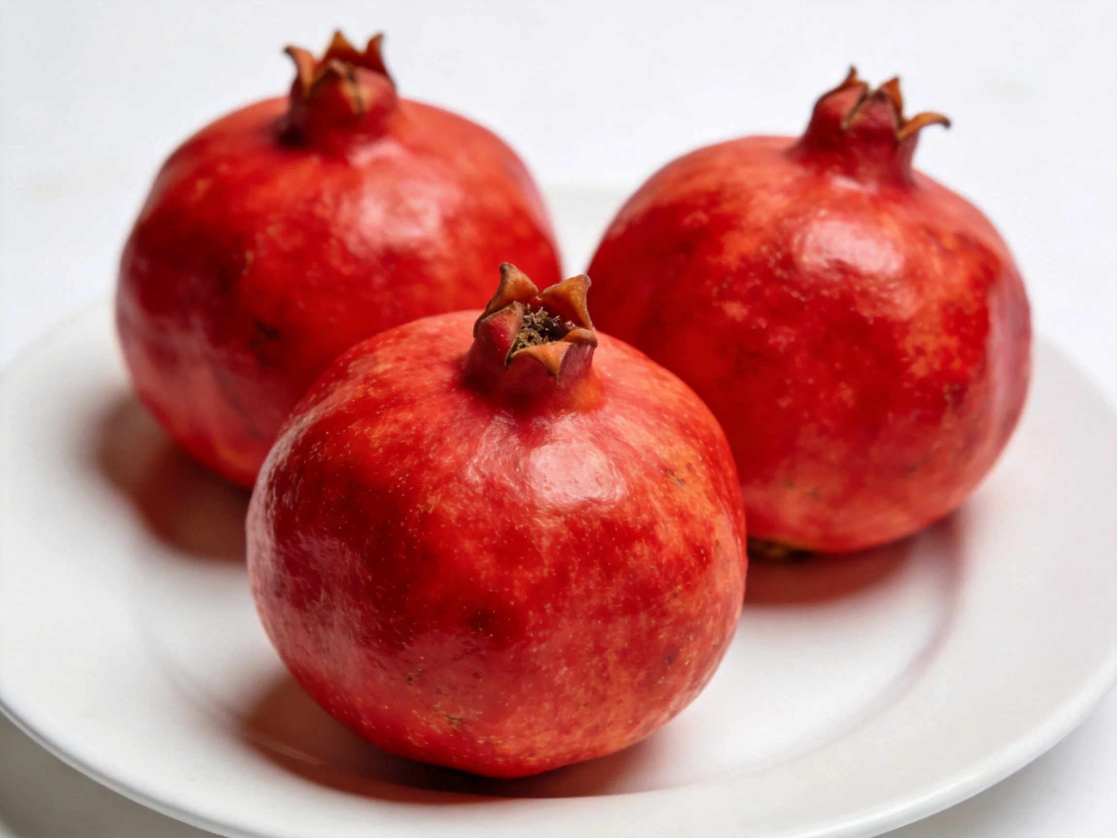 Three vibrant red pomegranates arranged on a white plate
