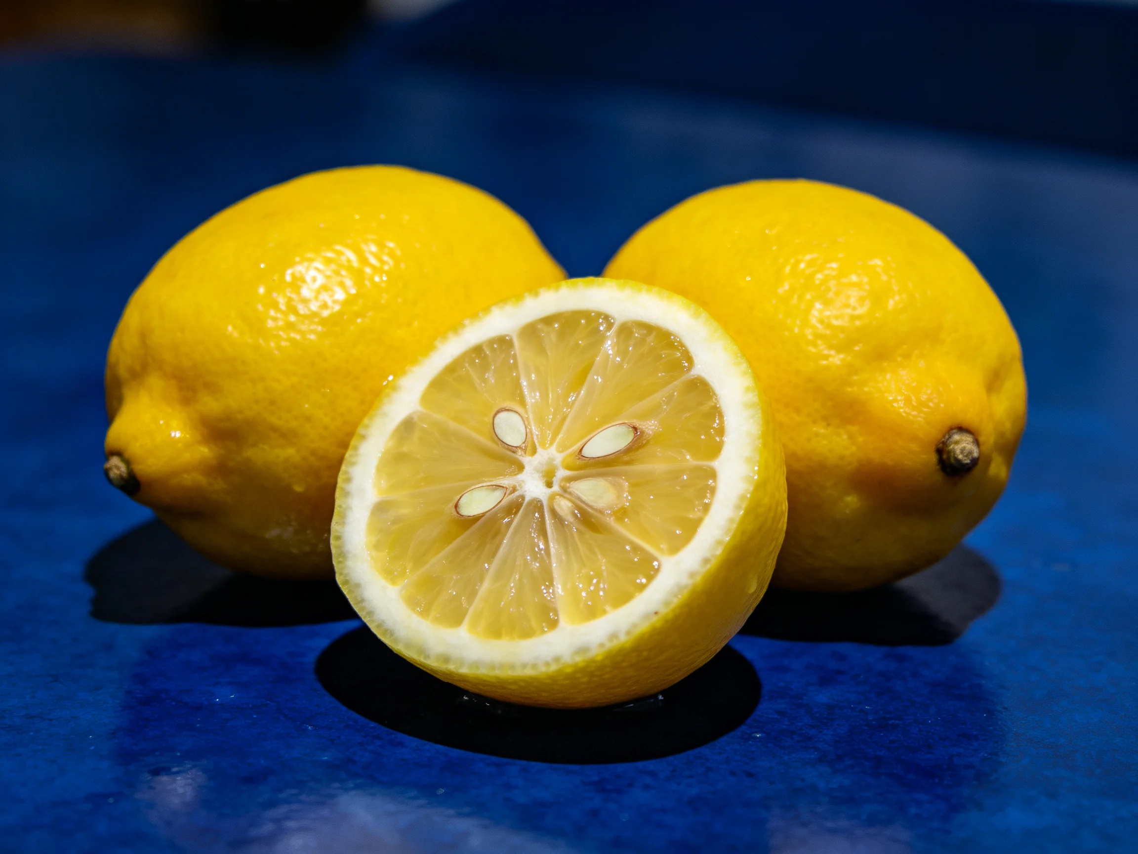 Three whole yellow lemons and one sliced lemon on a blue surface