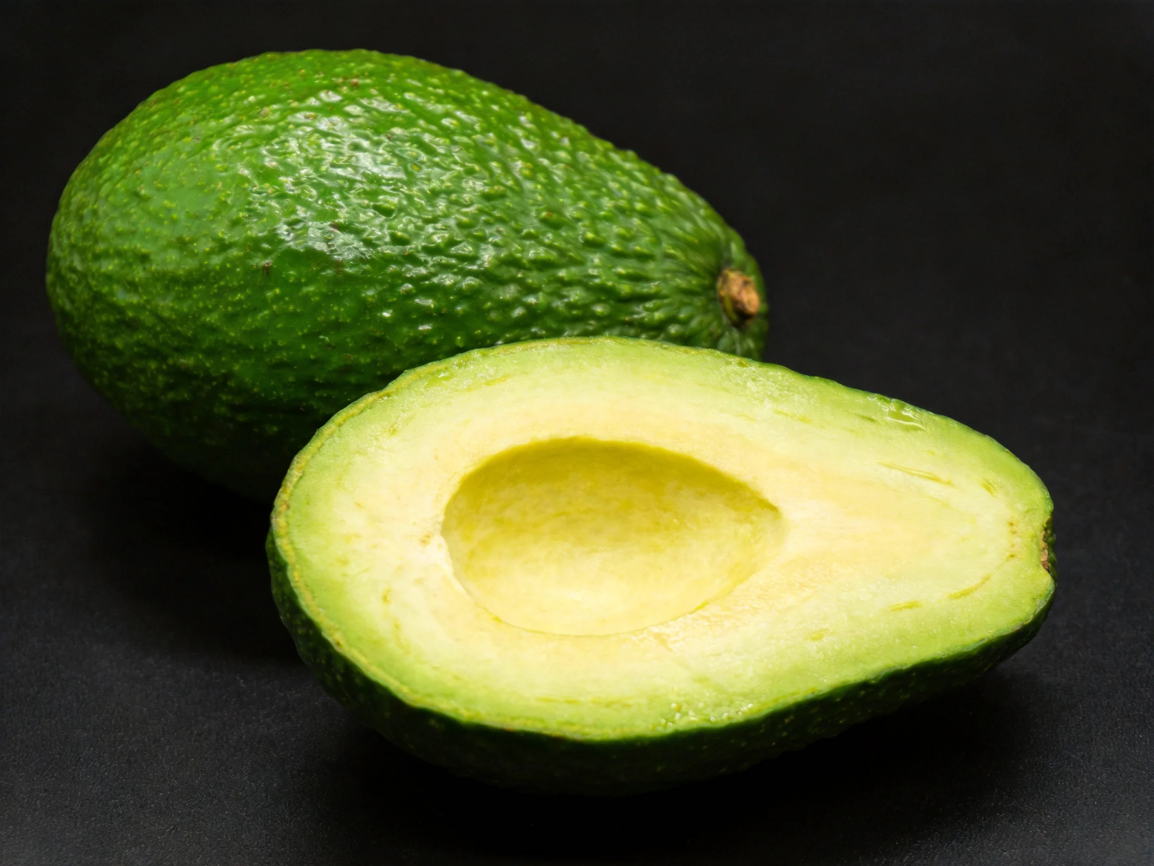 Two fresh green avocados, one whole and one halved