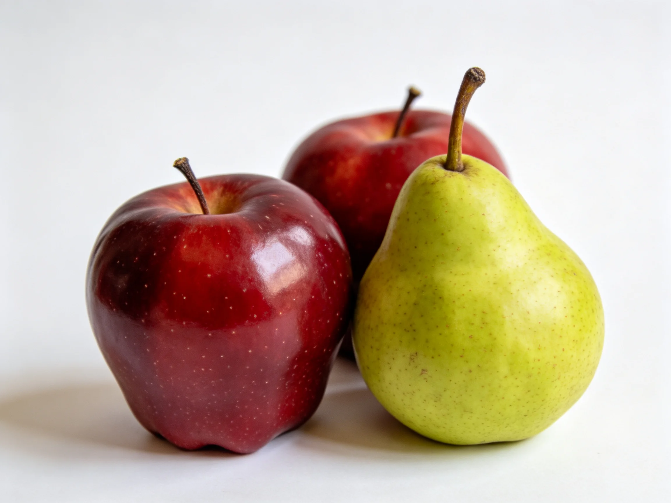 Two glossy red apples and a smooth green pear arranged closely