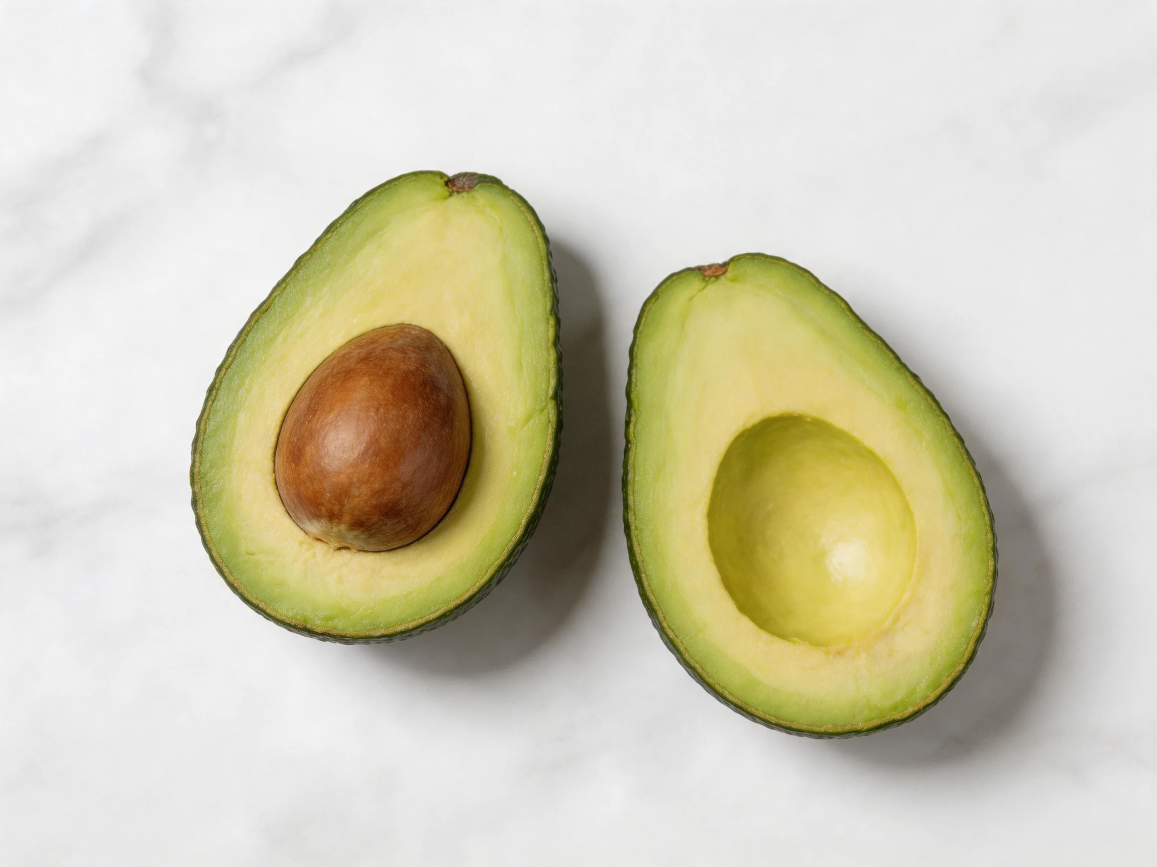 Two halved avocados reveal green flesh and brown seed