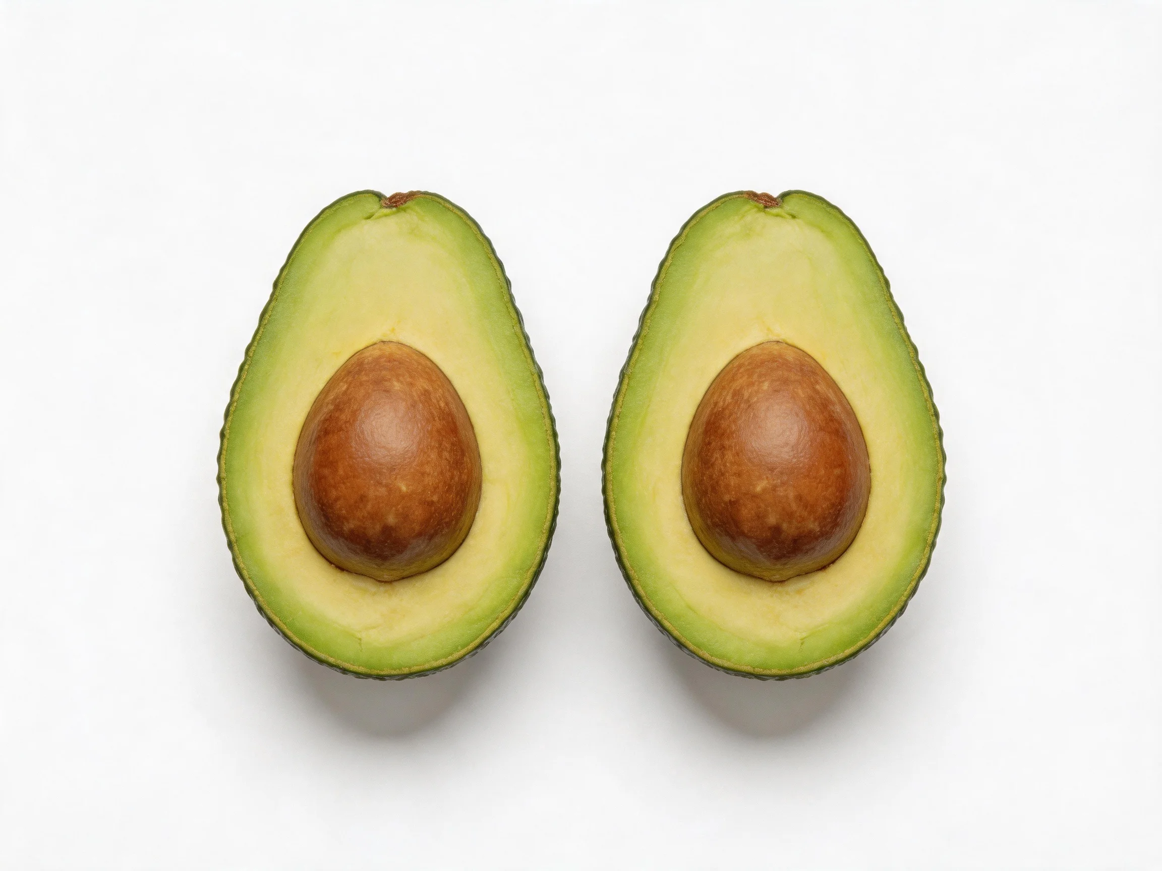 Two halved avocados with green flesh and brown pits