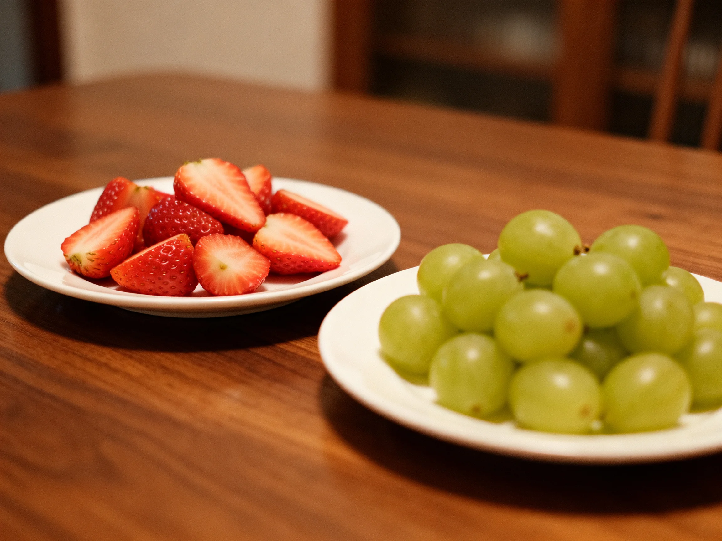 Two plates hold sliced strawberries and green grapes on a wooden table