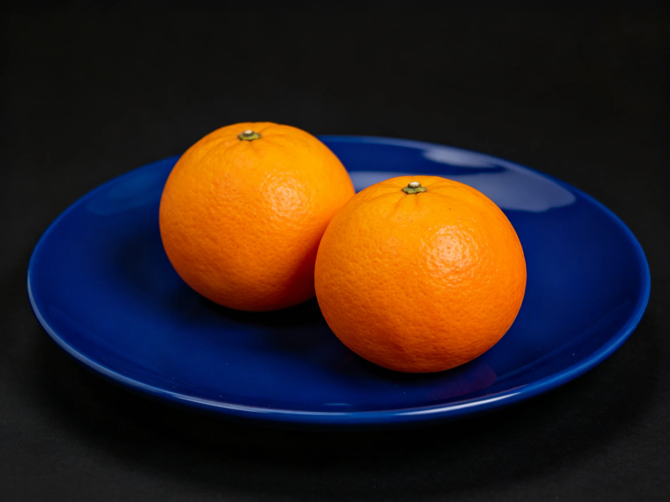 Two round oranges on a glossy blue plate with dark background
