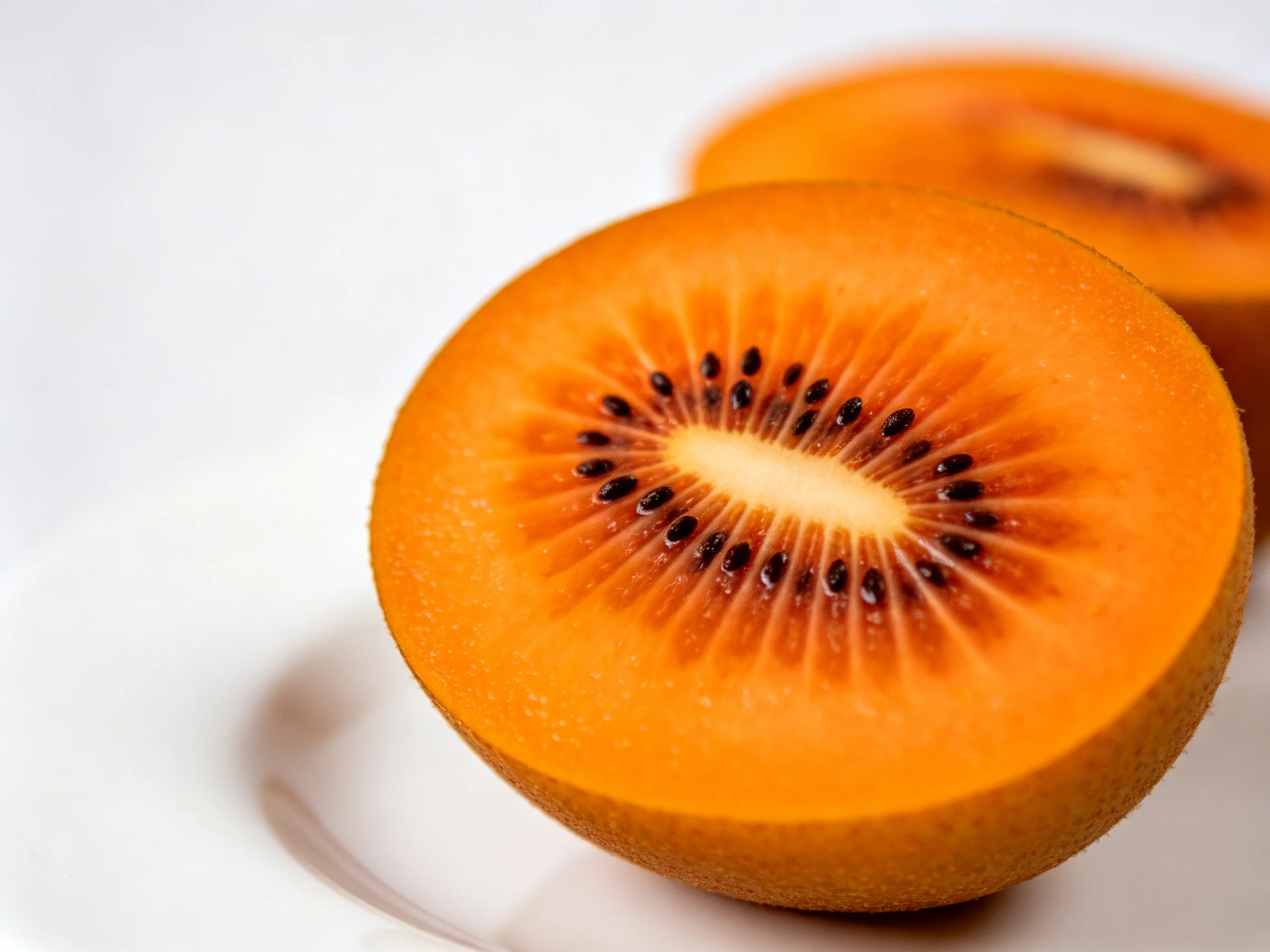 Two vibrant orange kiwi fruit halves displayed on a white surface
