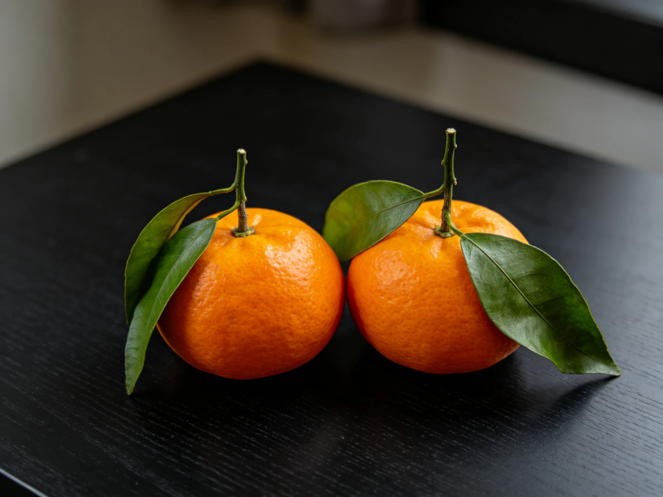 Two vibrant oranges with green leaves rest on a dark wooden surface.