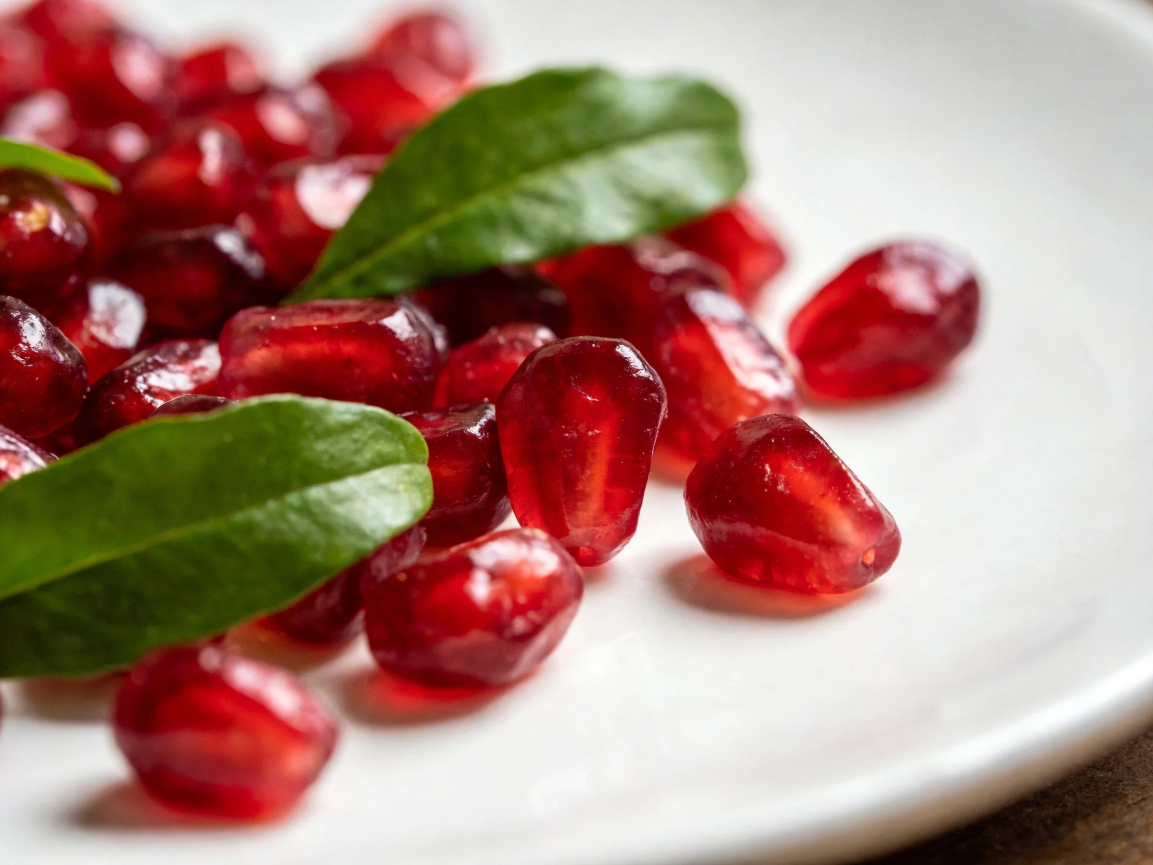 Vibrant red pomegranate seeds with fresh green leaves on a white plate