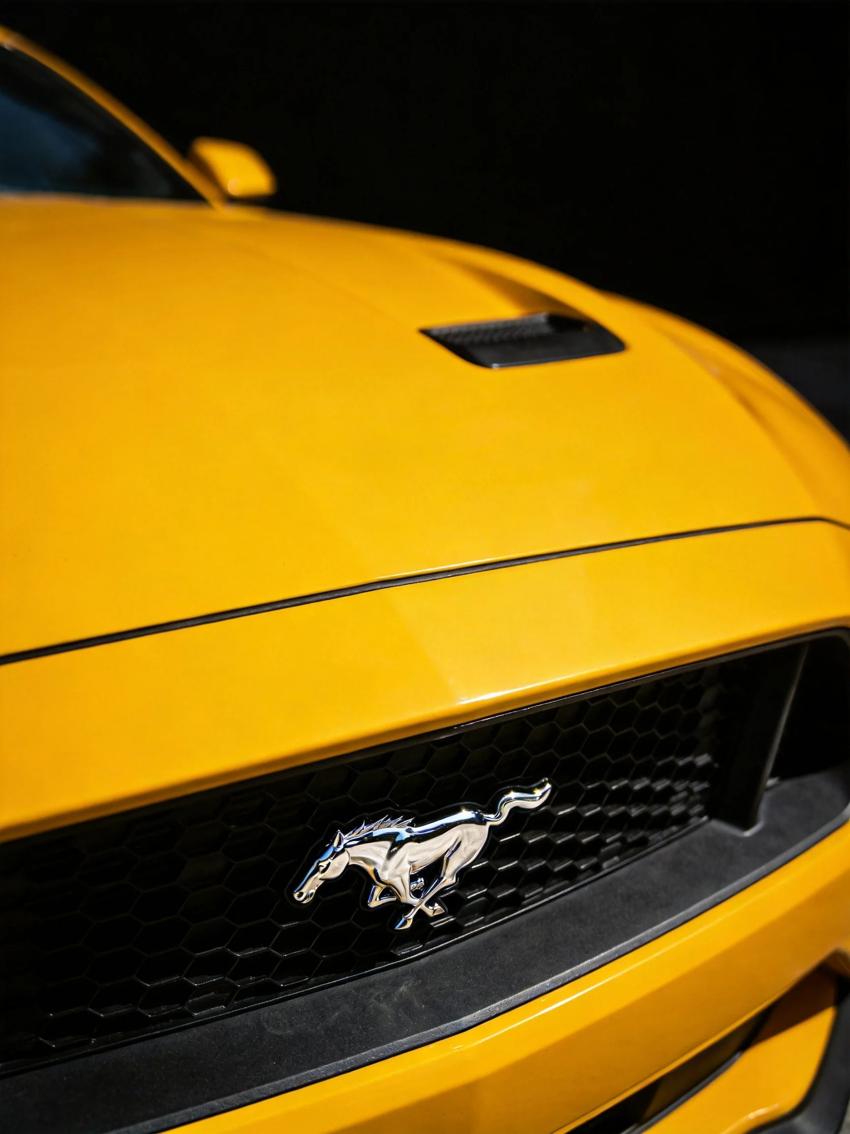 A bright yellow sports car displaying a polished silver horse emblem