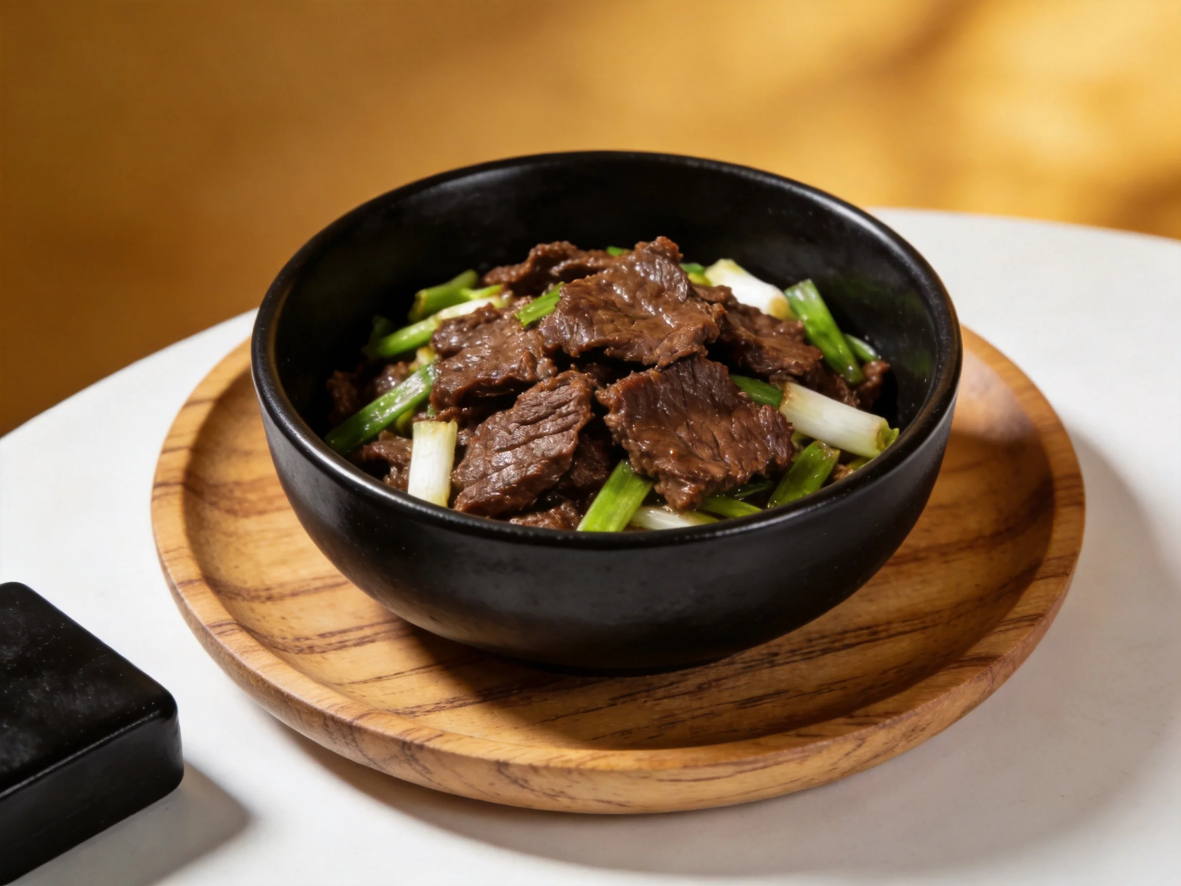 A black bowl filled with savory beef stir - fry and scallion slices