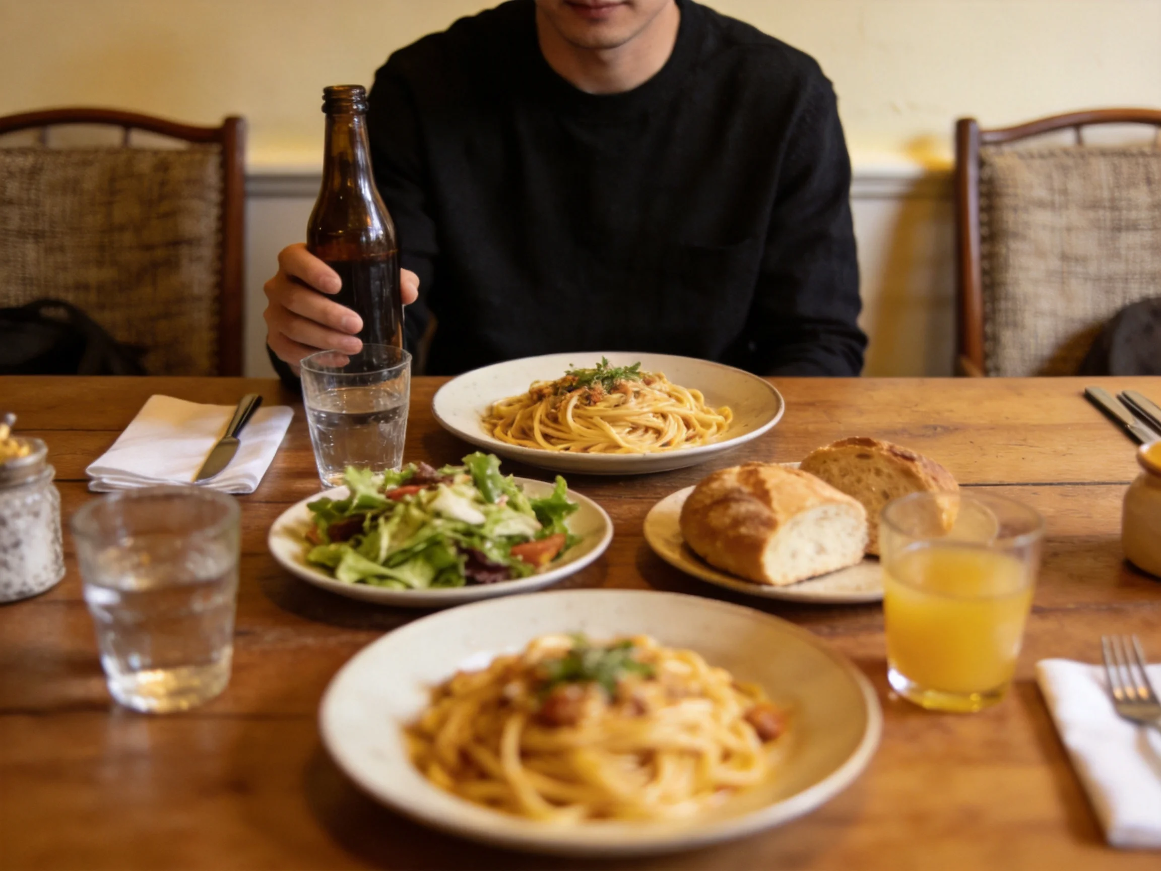 A cozy wooden table with pasta, salad, bread, and drinks