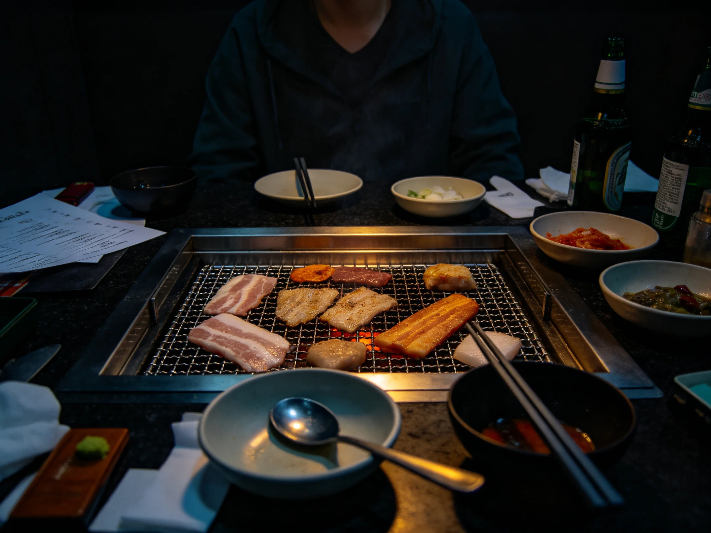 A dimly lit restaurant table with a grill of assorted grilled meats and side dishes