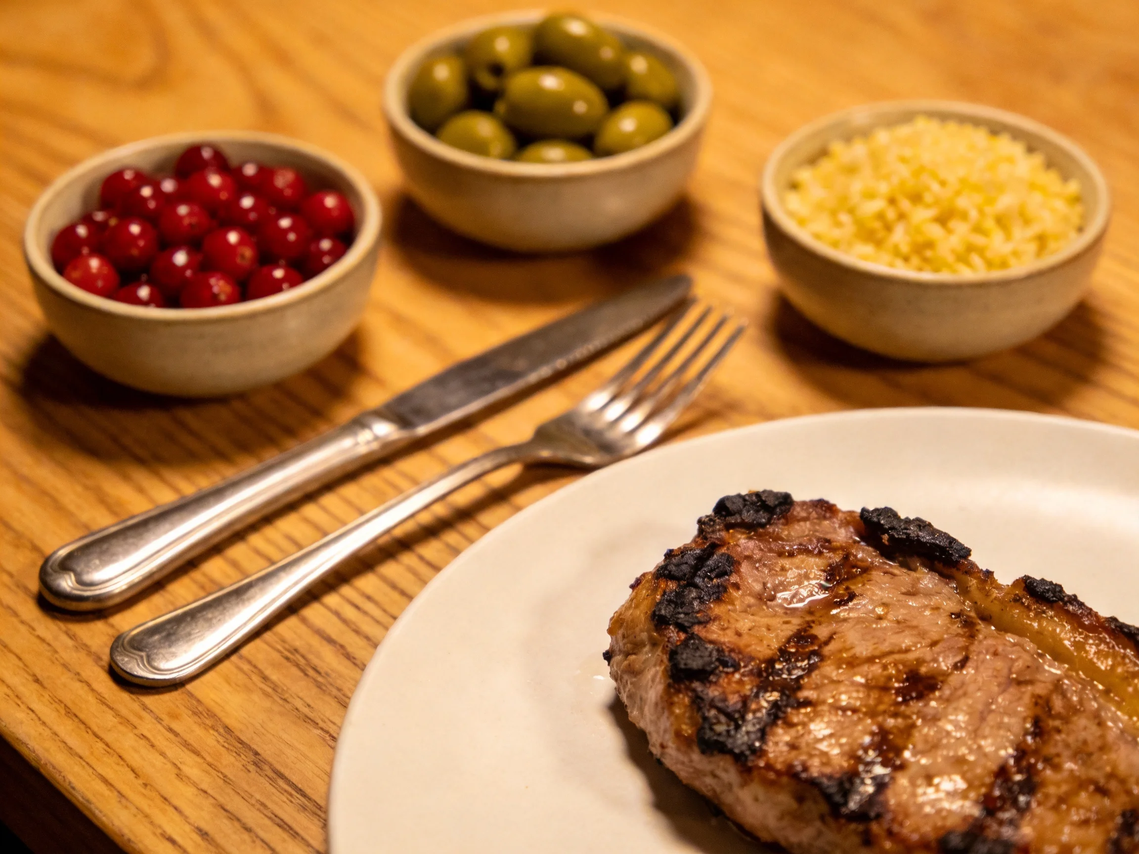 A grilled steak served with three bowls of cranberries, olives, and cheese