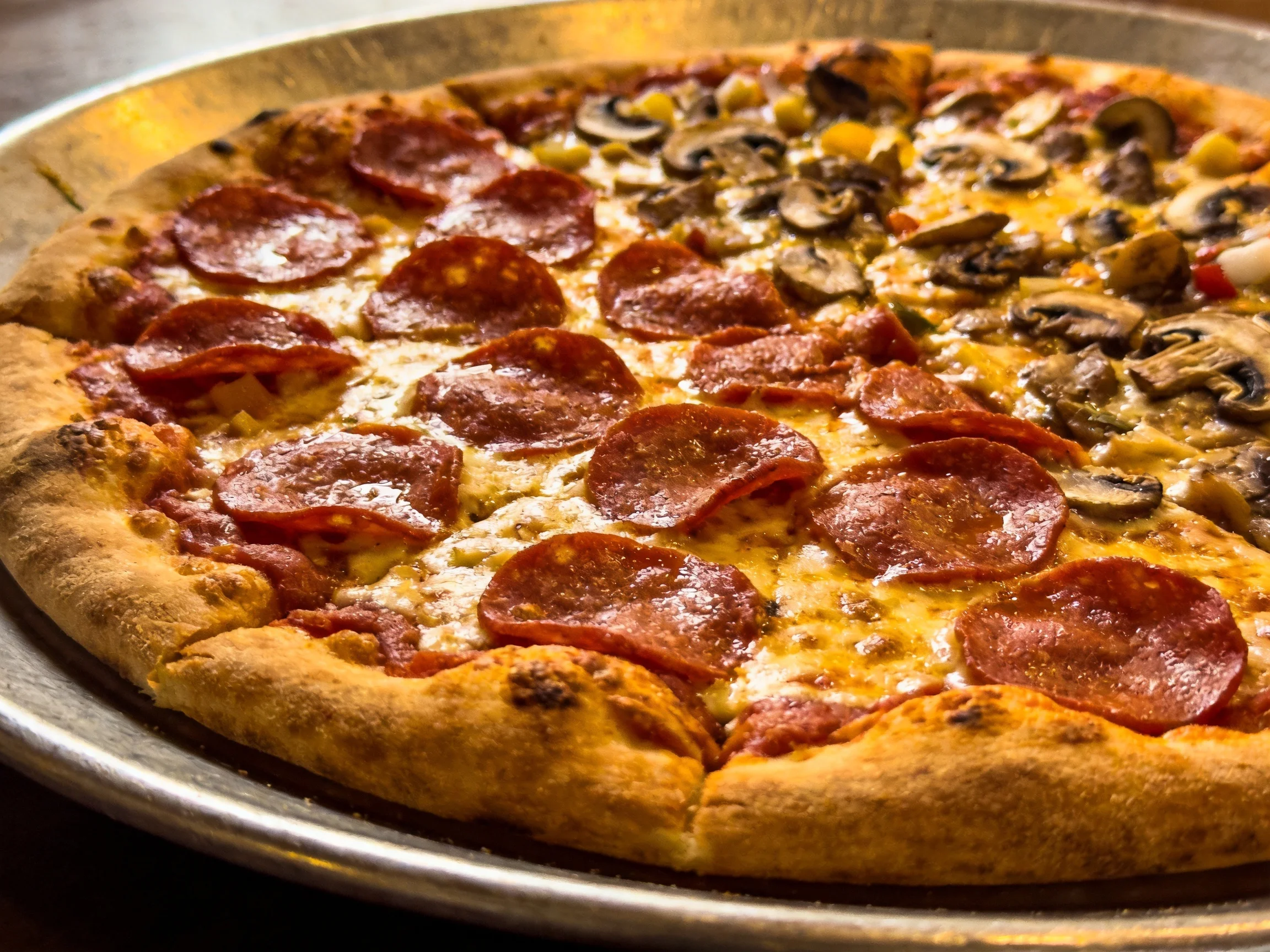 A half - and - half pepperoni and mushroom pizza on a metal tray