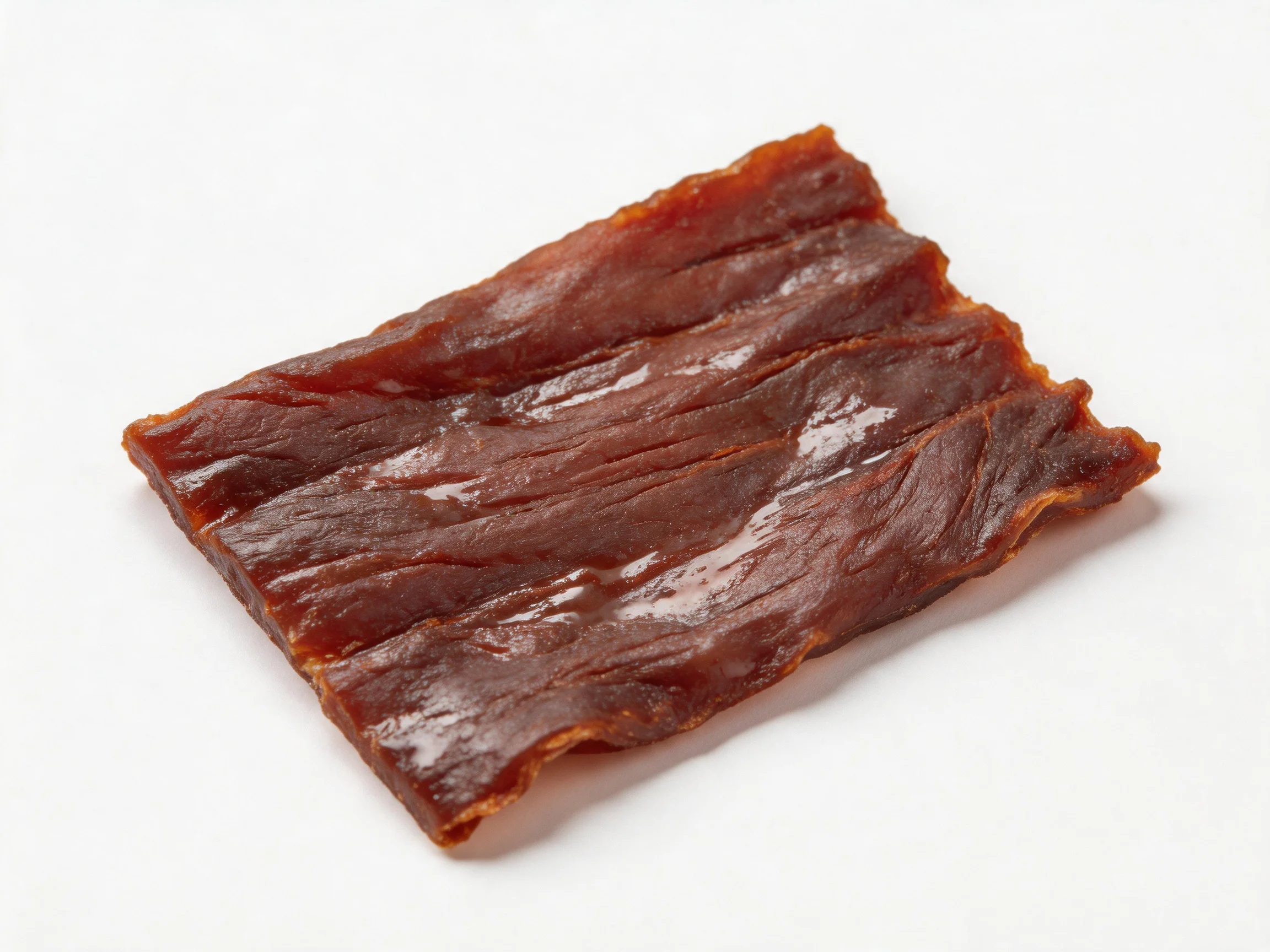 A rectangular slice of dark brown, glossy dried meat on a white surface