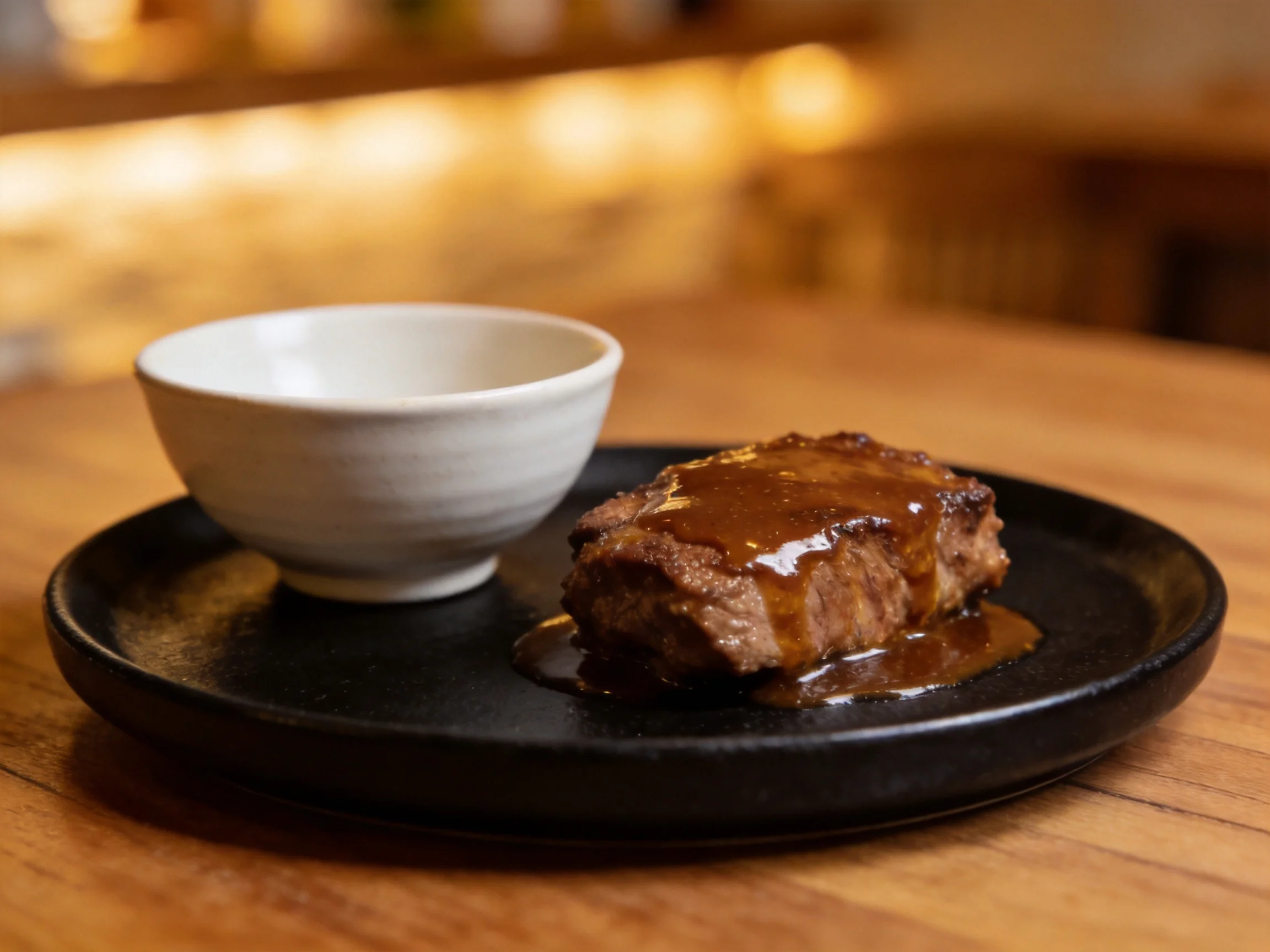A savory steak drizzled with brown sauce beside a white bowl