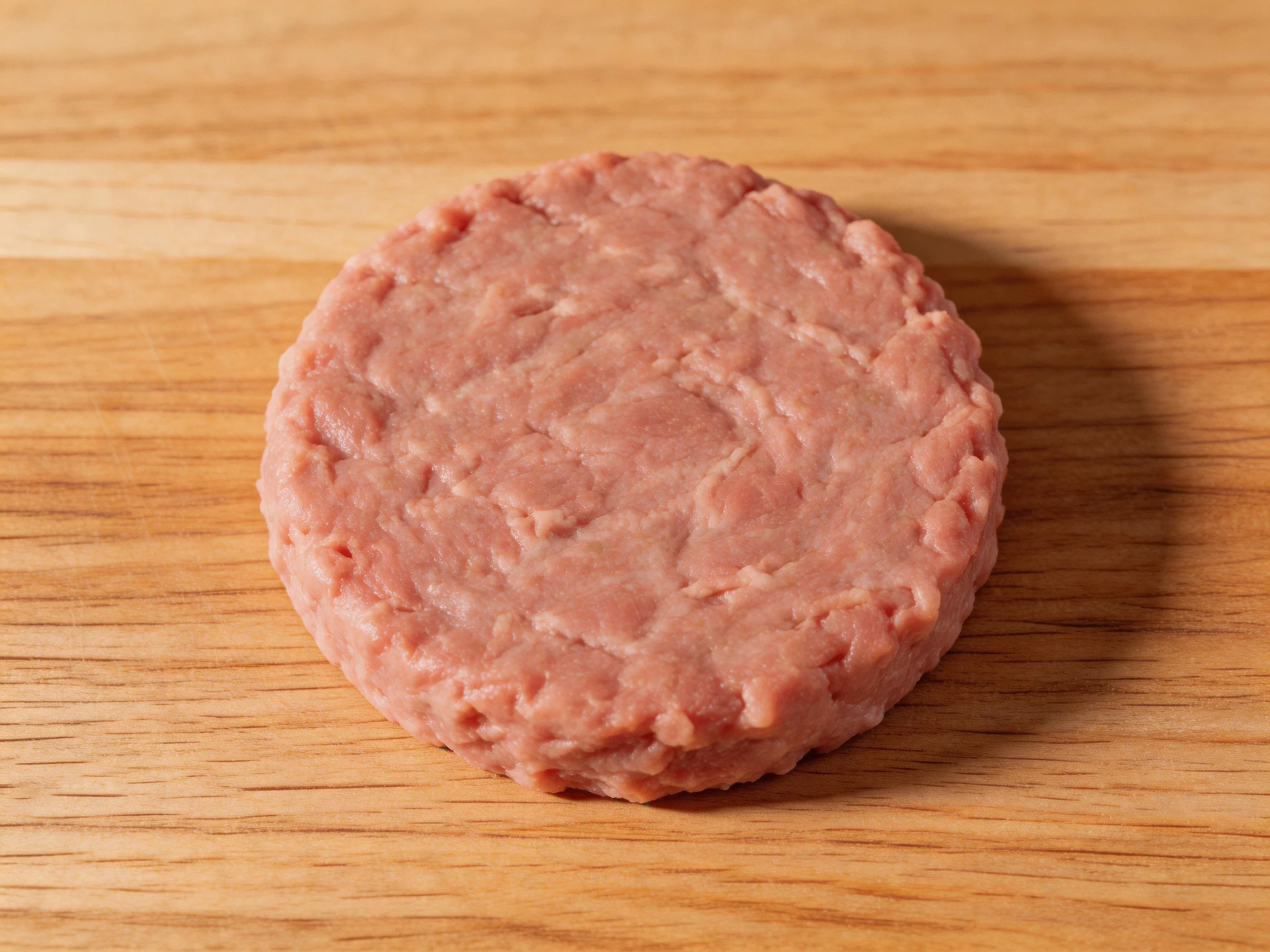 A single round raw hamburger patty on a wooden cutting board
