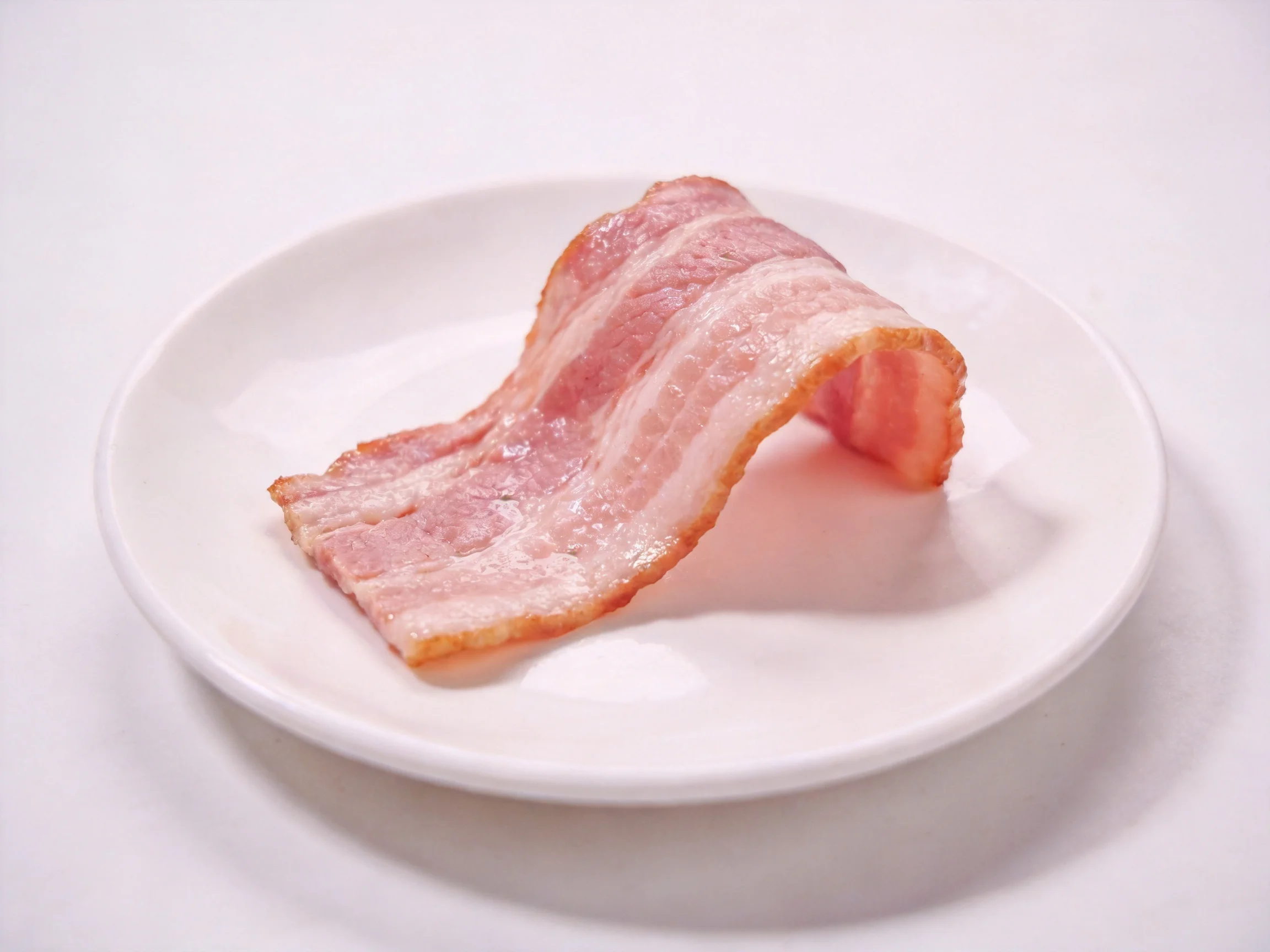 A single strip of cooked bacon rests on a plain white plate