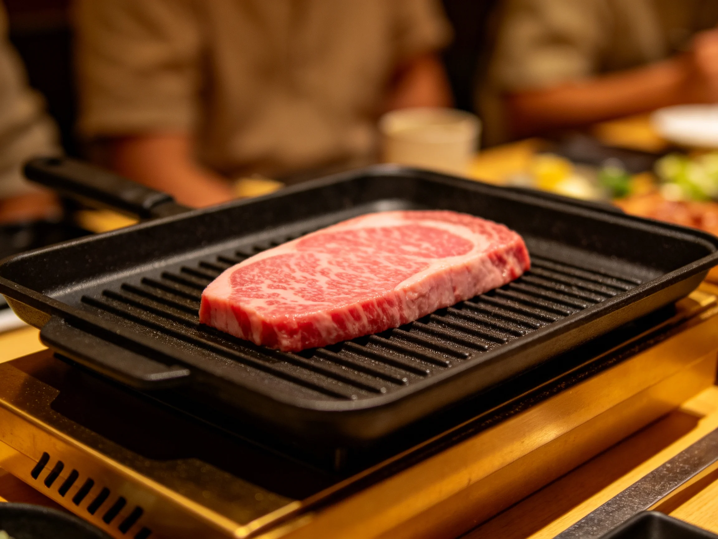 A thick slice of marbled beef grilling on a black cast iron pan