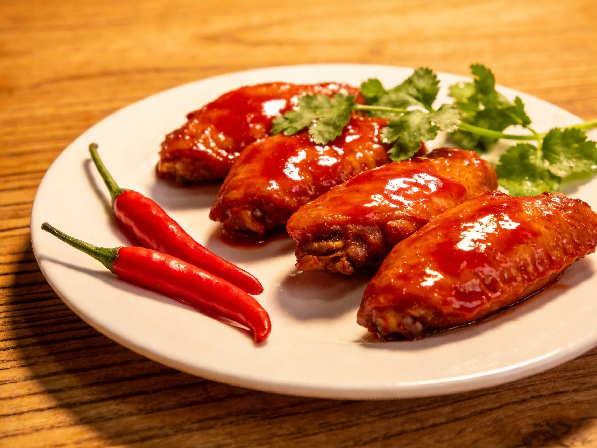 Four glossy chicken wings with red chili and cilantro garnish