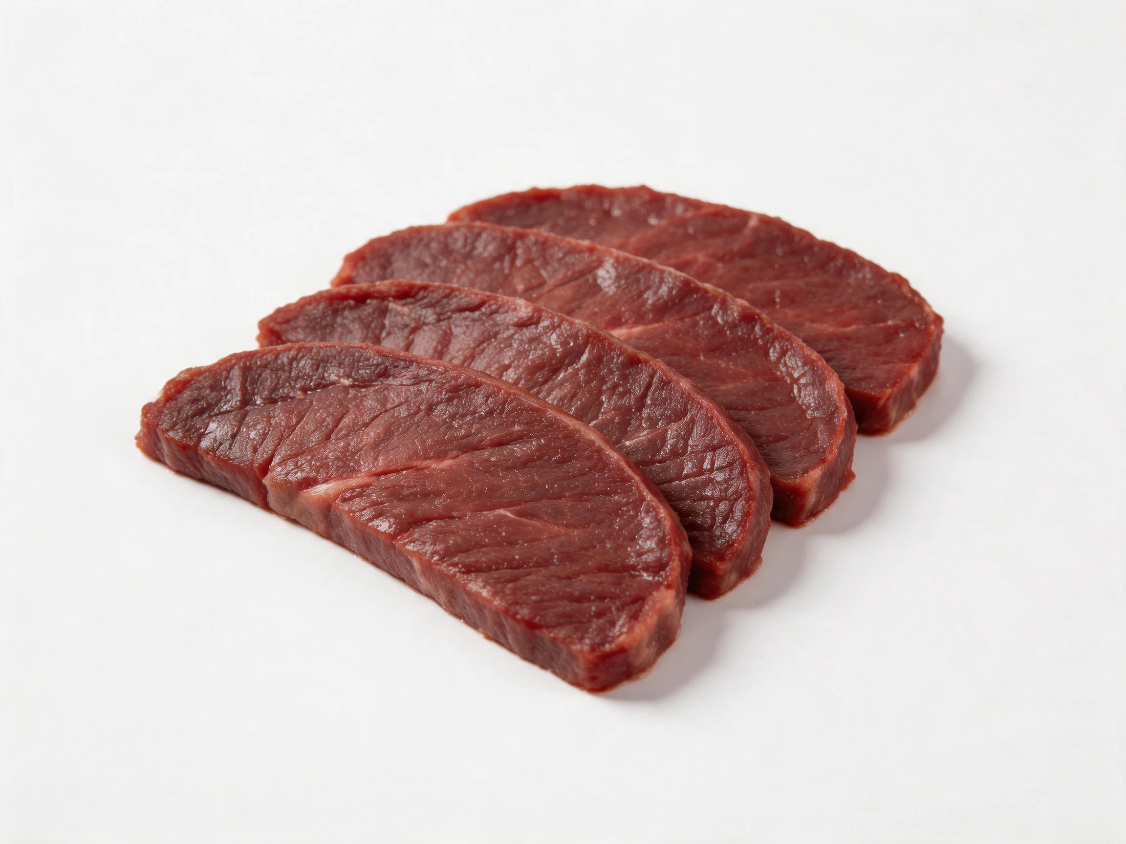 Four thick slices of maroon raw beef arranged on a white surface