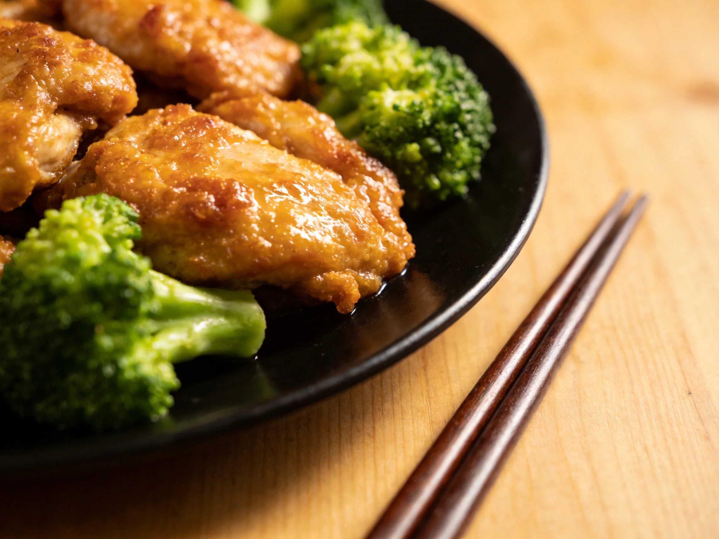 Golden-brown chicken wings with vibrant green broccoli on a black plate