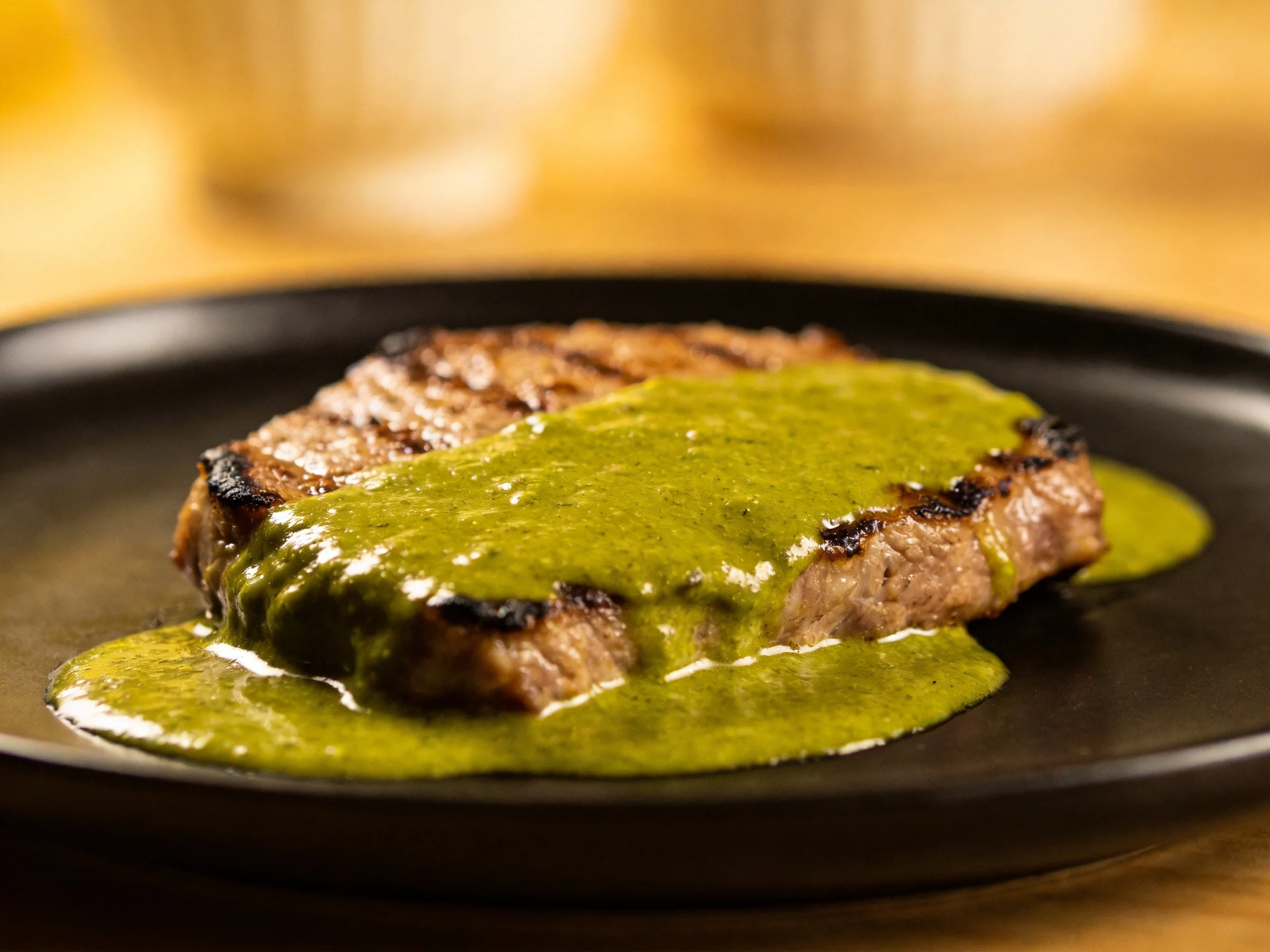 Grilled steak topped with vivid green sauce on a dark plate