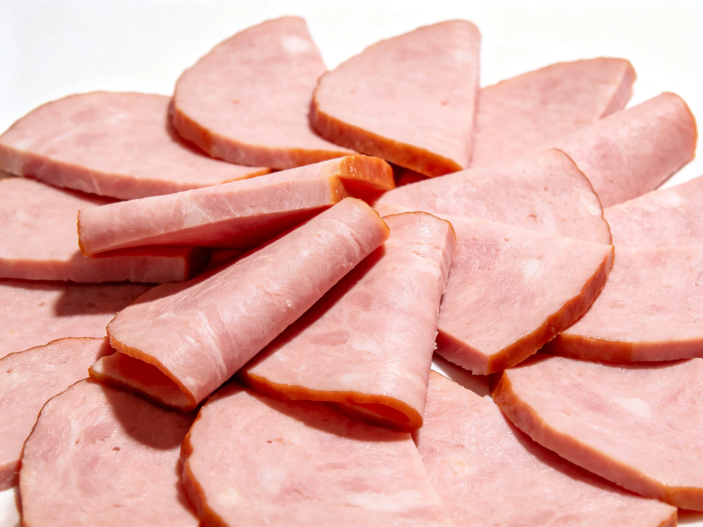 Many thin slices of pink deli ham arranged closely together.