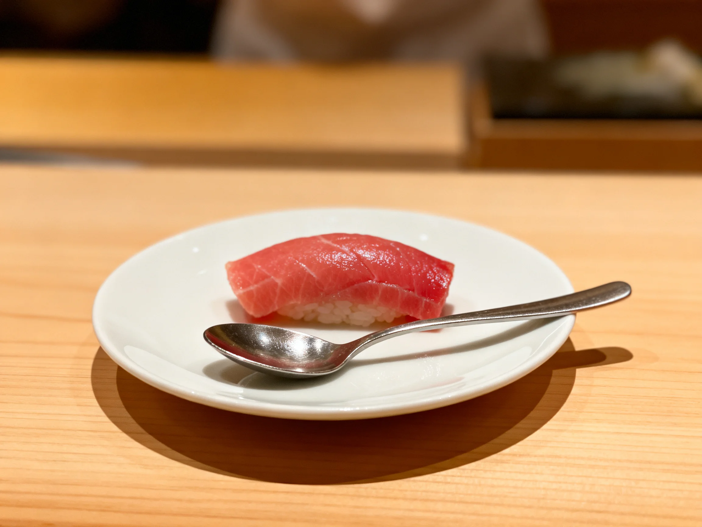 Single piece of tuna nigiri sushi on white dish with metal spoon