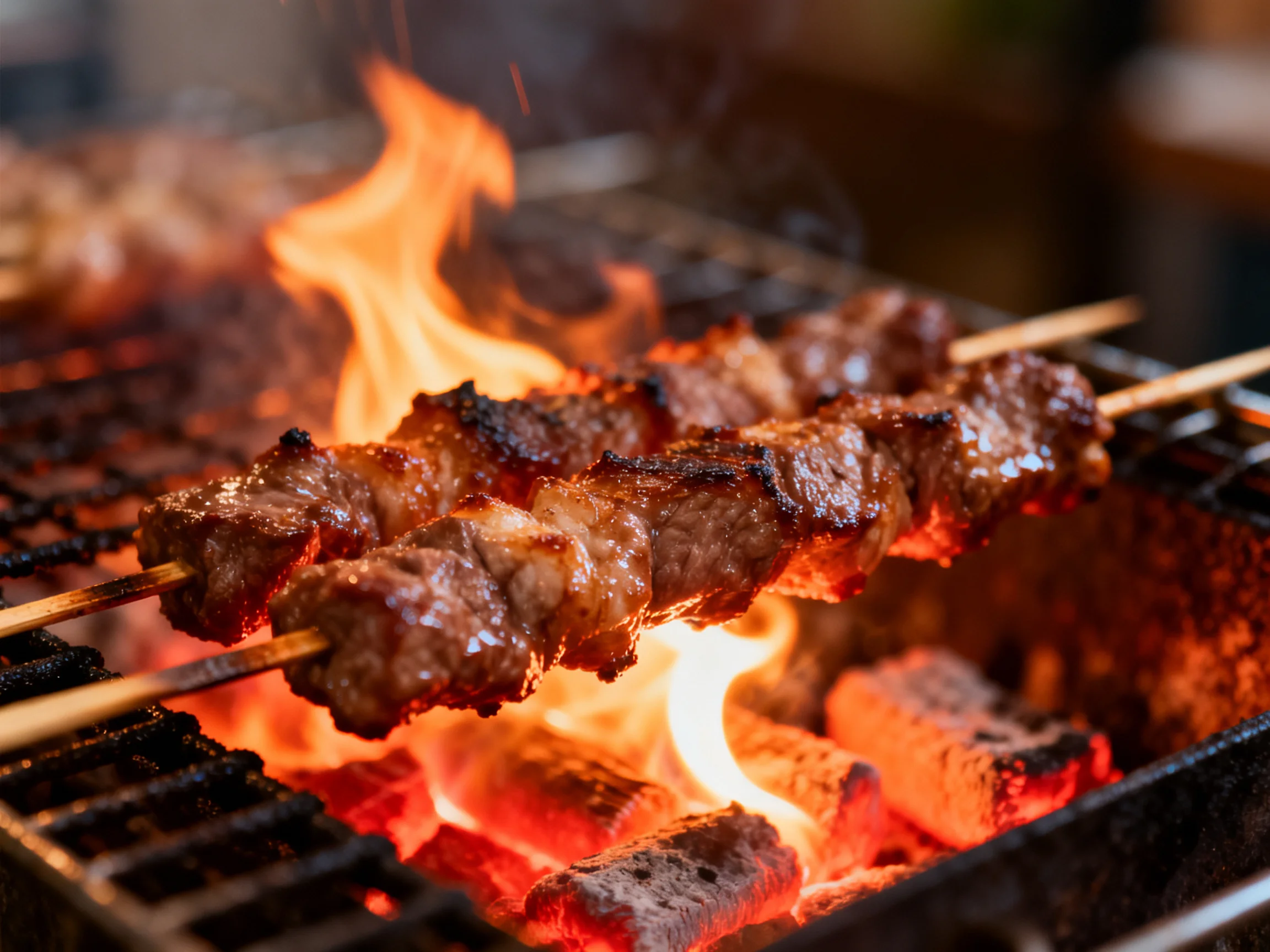 Skewered meats barbecue over bright orange flames on a charcoal grill