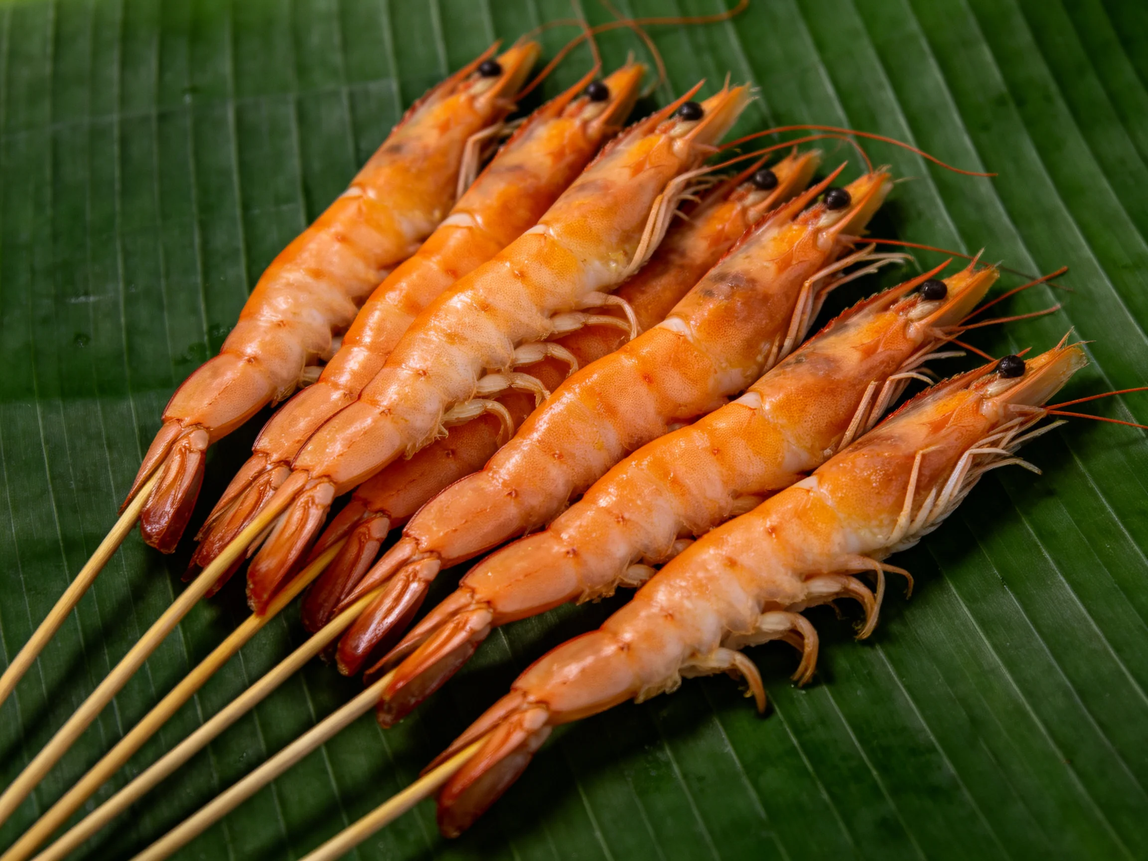 Skewered orange shrimp arranged on a green banana leaf