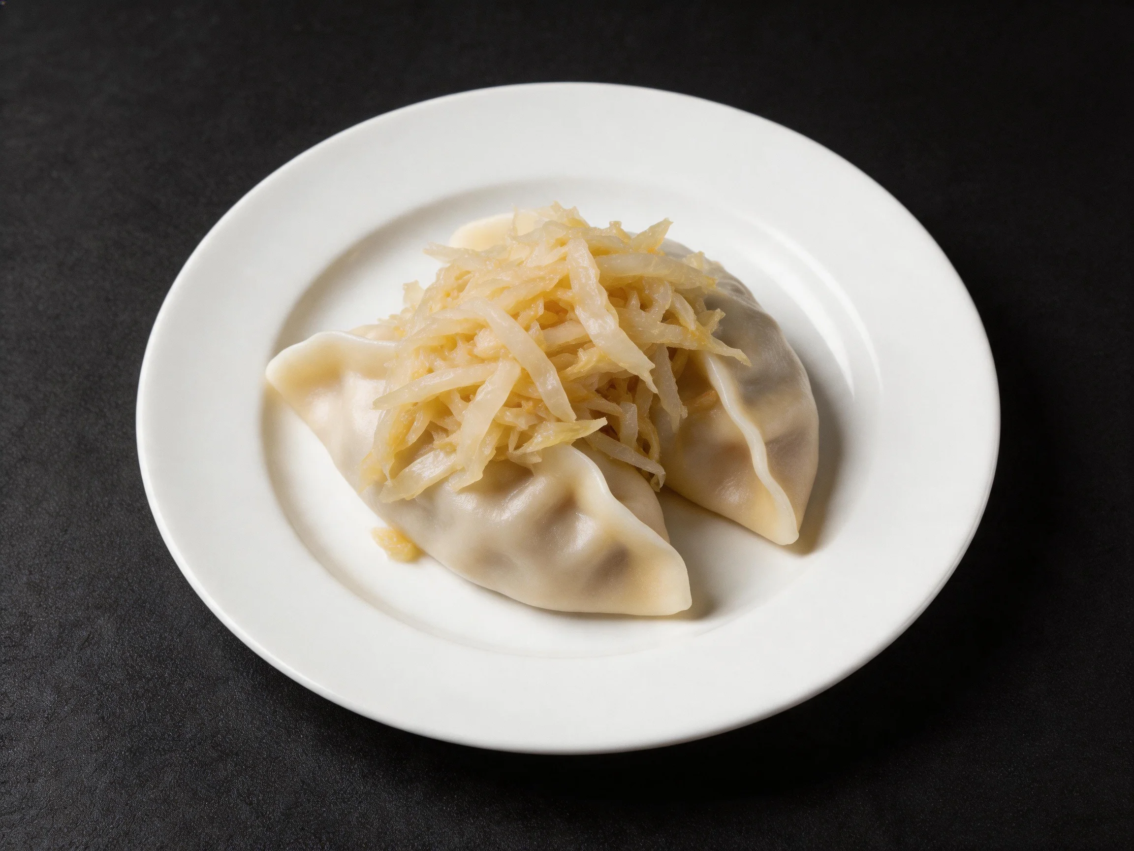 Two dumplings topped with shredded sauerkraut on a white plate