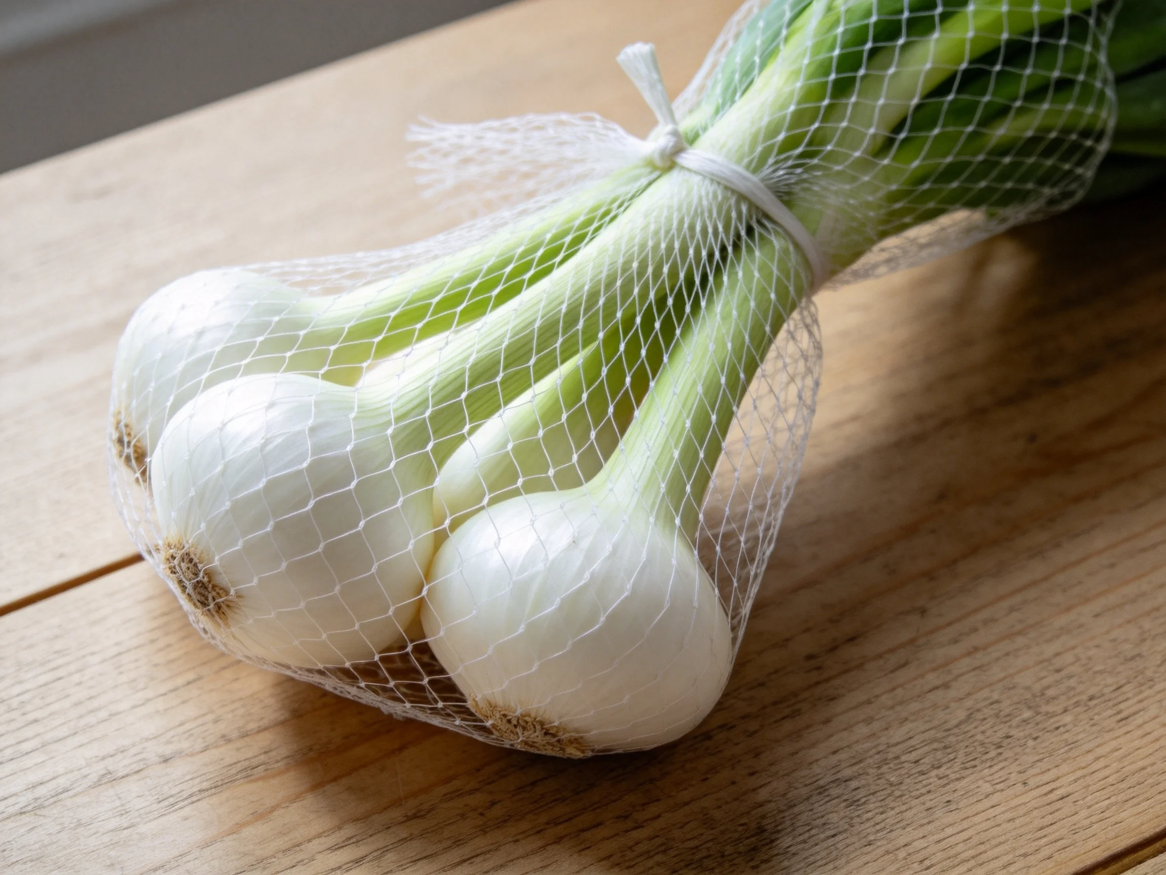 A bundle of fresh white onions wrapped in mesh netting on a wooden surface