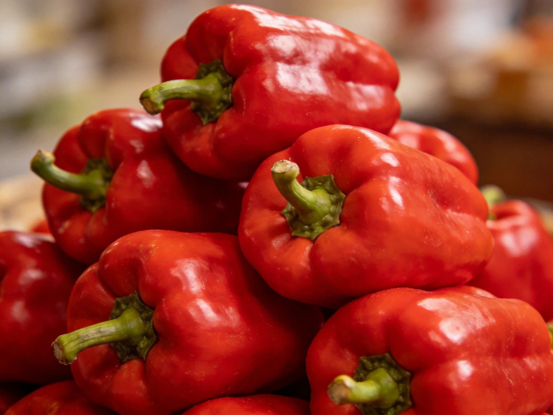 A close-up view of numerous vibrant red bell peppers stacked together