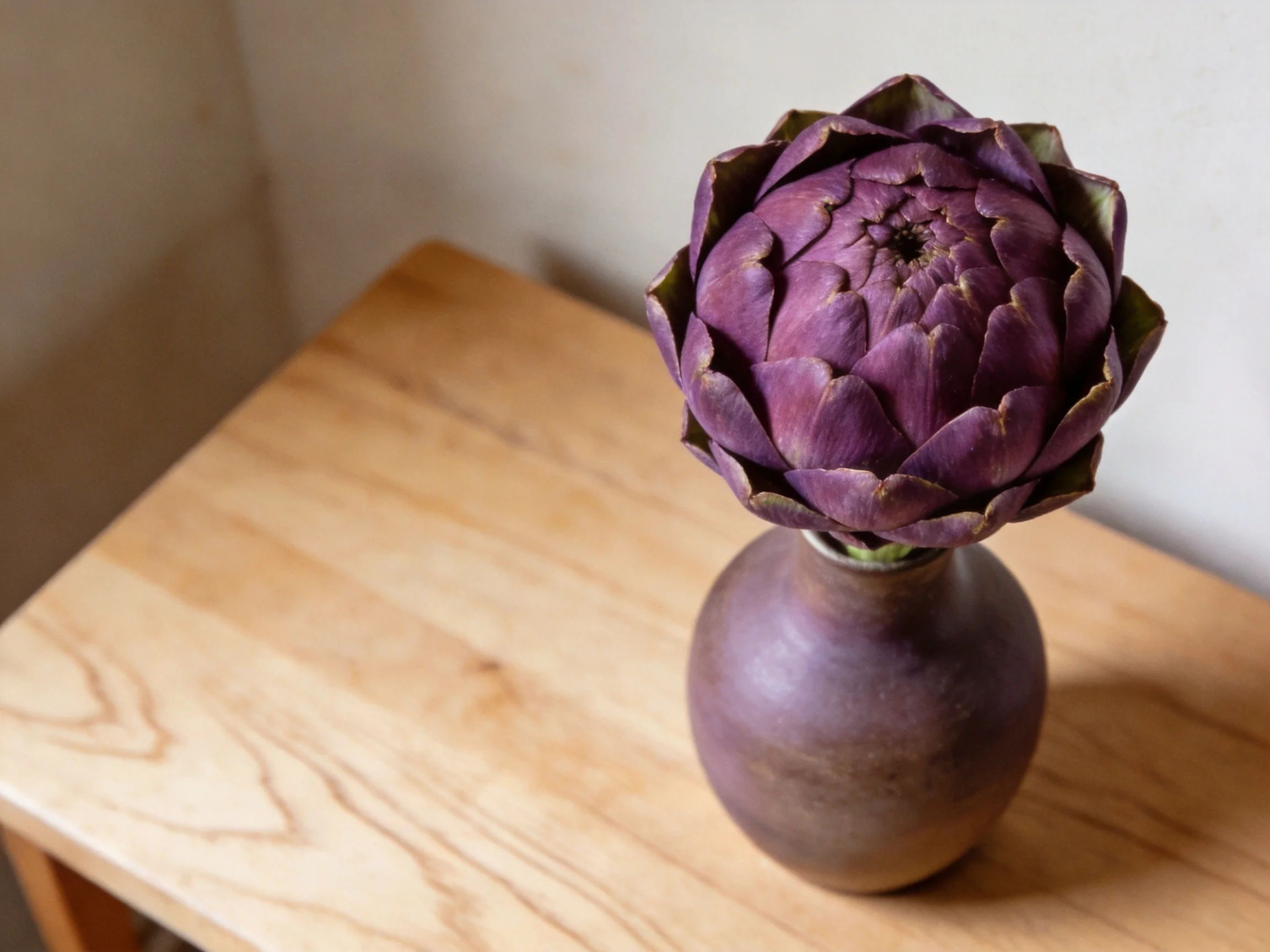 A deep purple artichoke flower in a brown vase on a wooden table