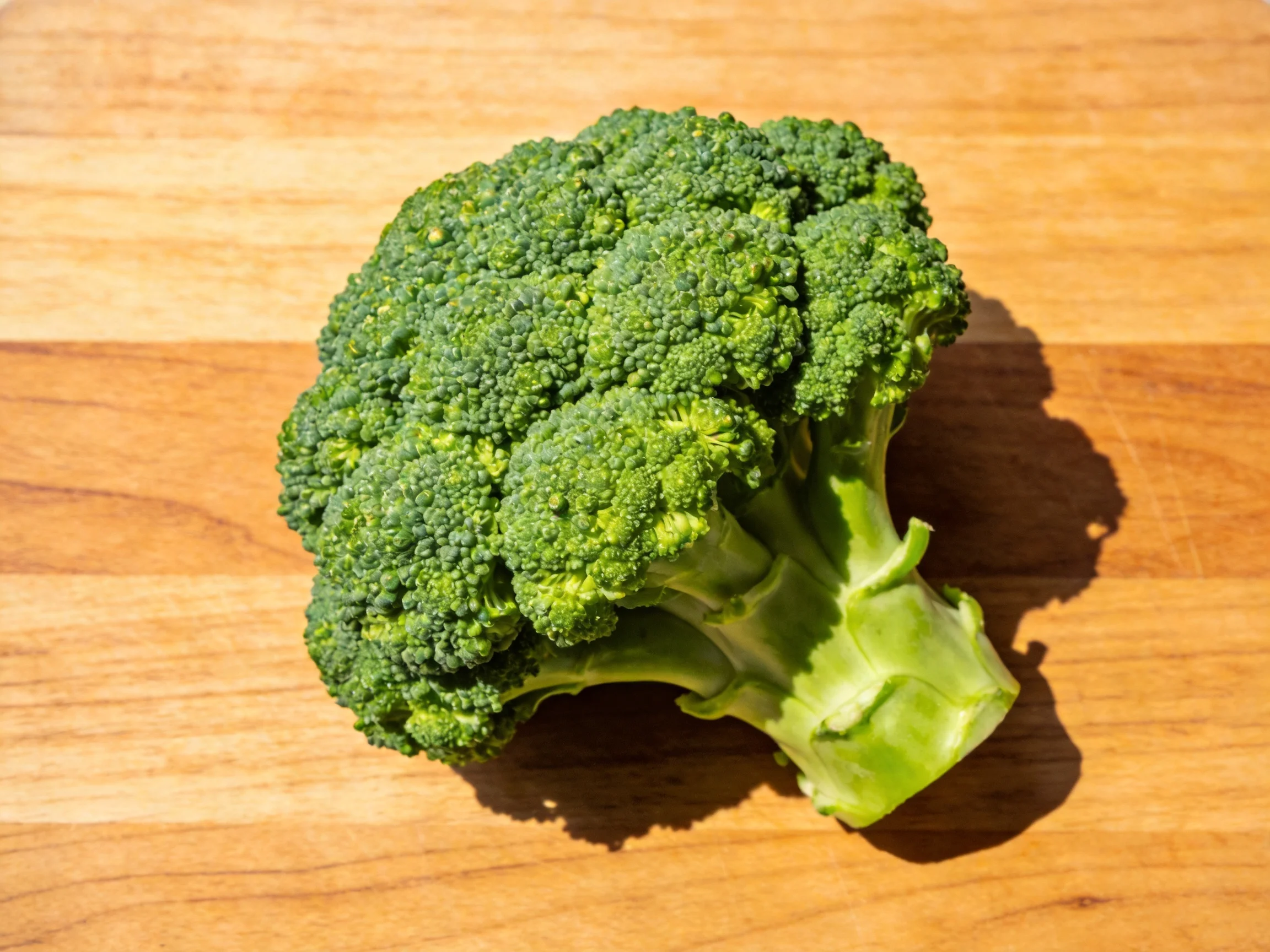 A fresh green broccoli head rests on a smooth wooden cutting board