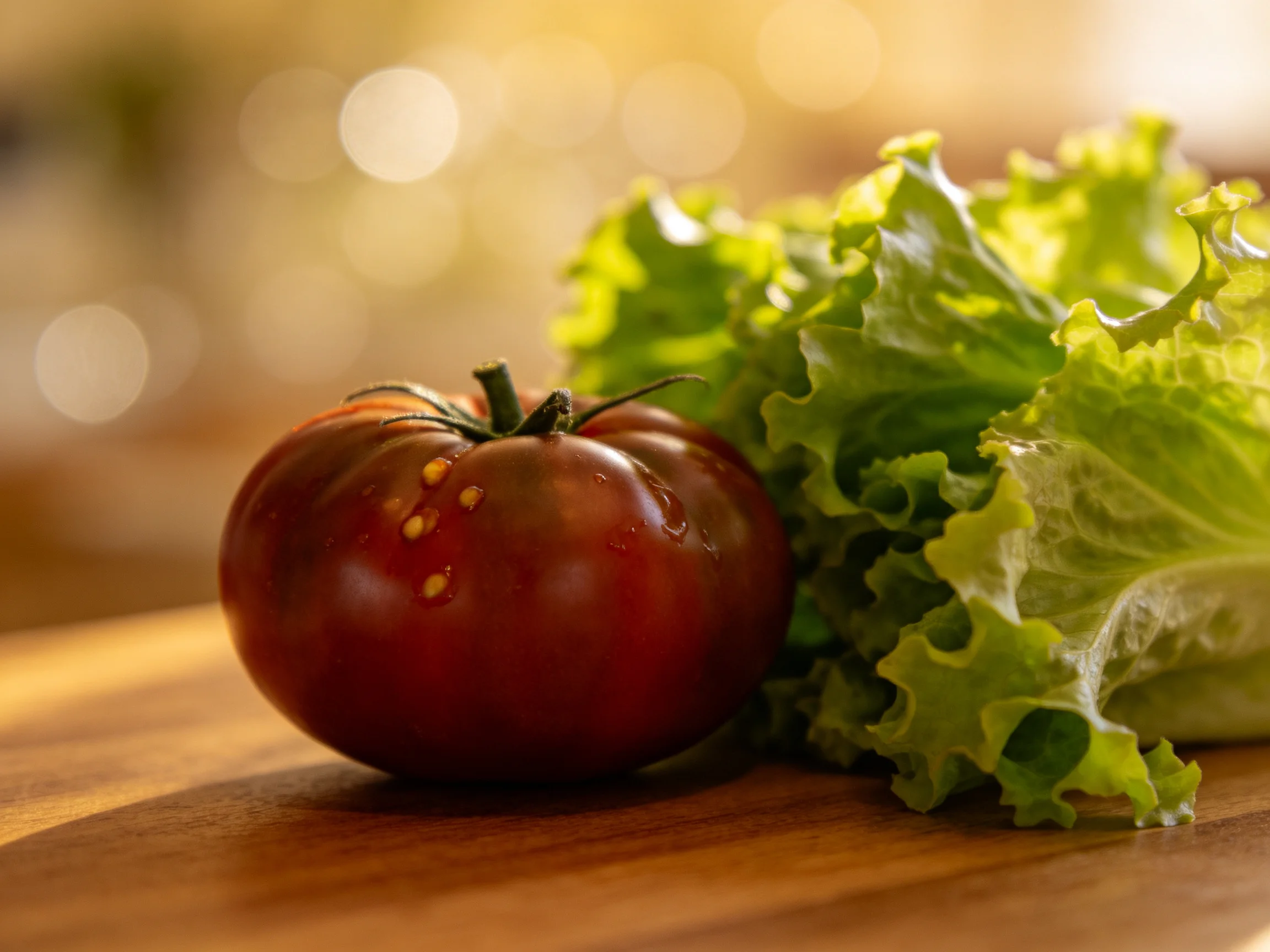 A glossy dark red tomato beside fresh green lettuce on a wooden cuttingboard