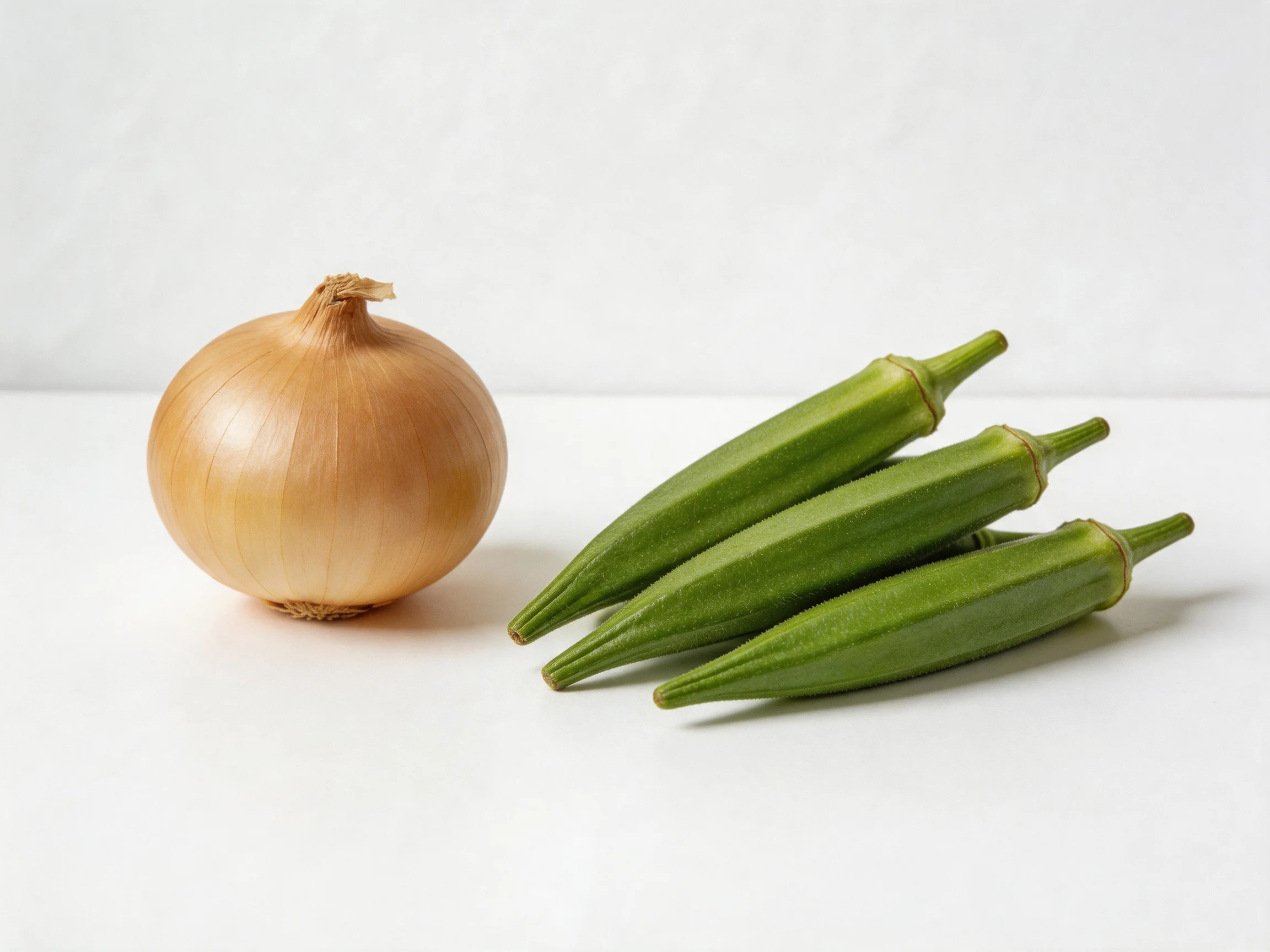 A golden-brown onion alongside three green okras on a white surface
