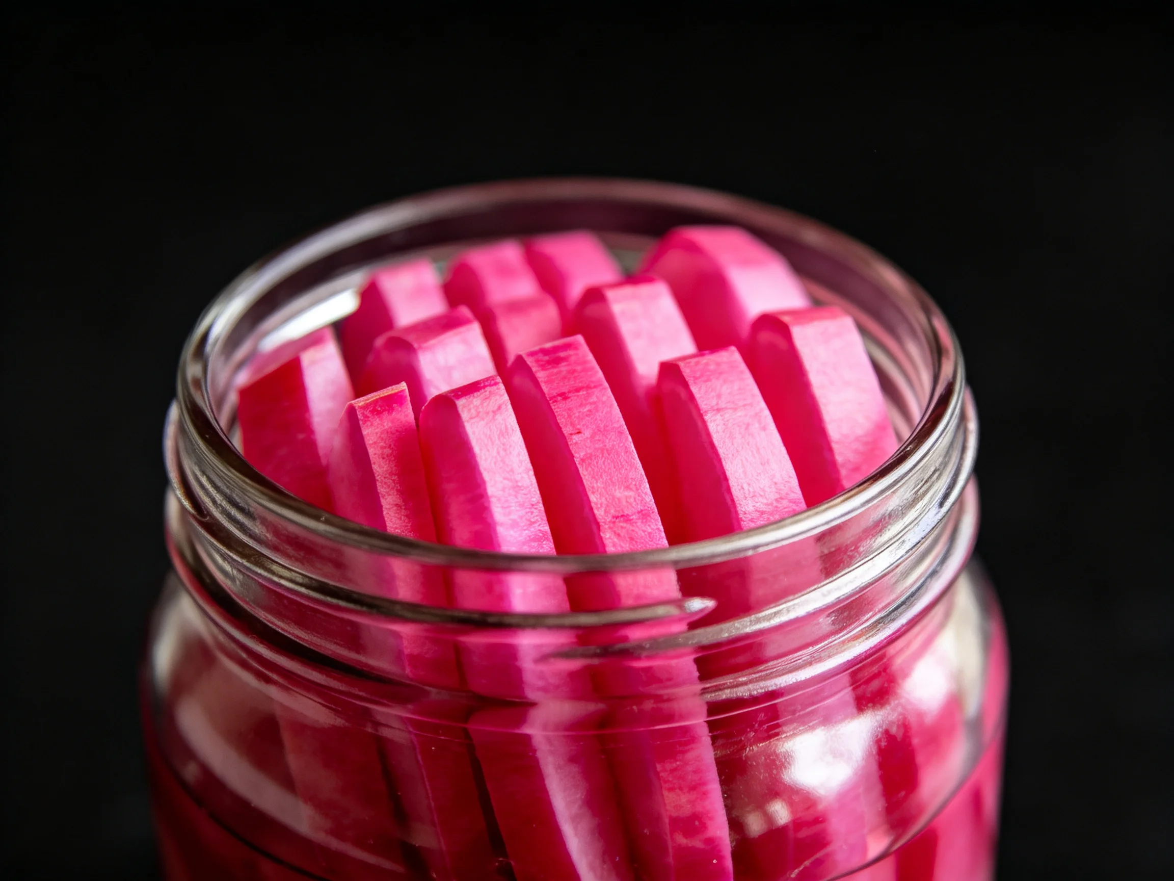 A jar holds vibrant pink pickled radish slices