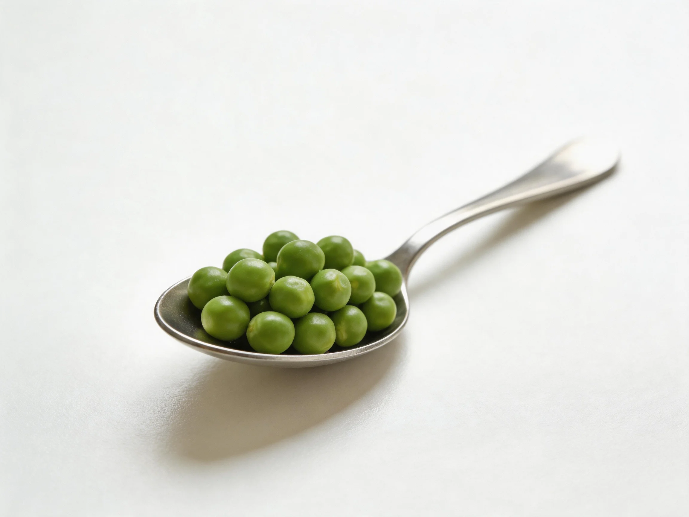 A metal spoon holds a cluster of fresh green peas