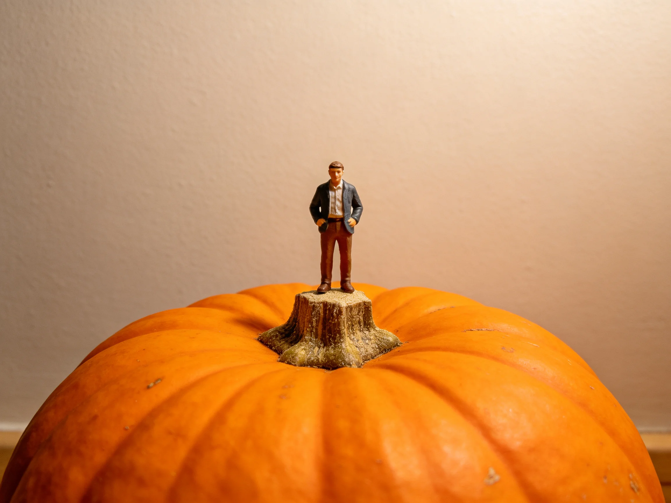 A miniature man figurine stands on a tree stump atop a large orange pumpkin