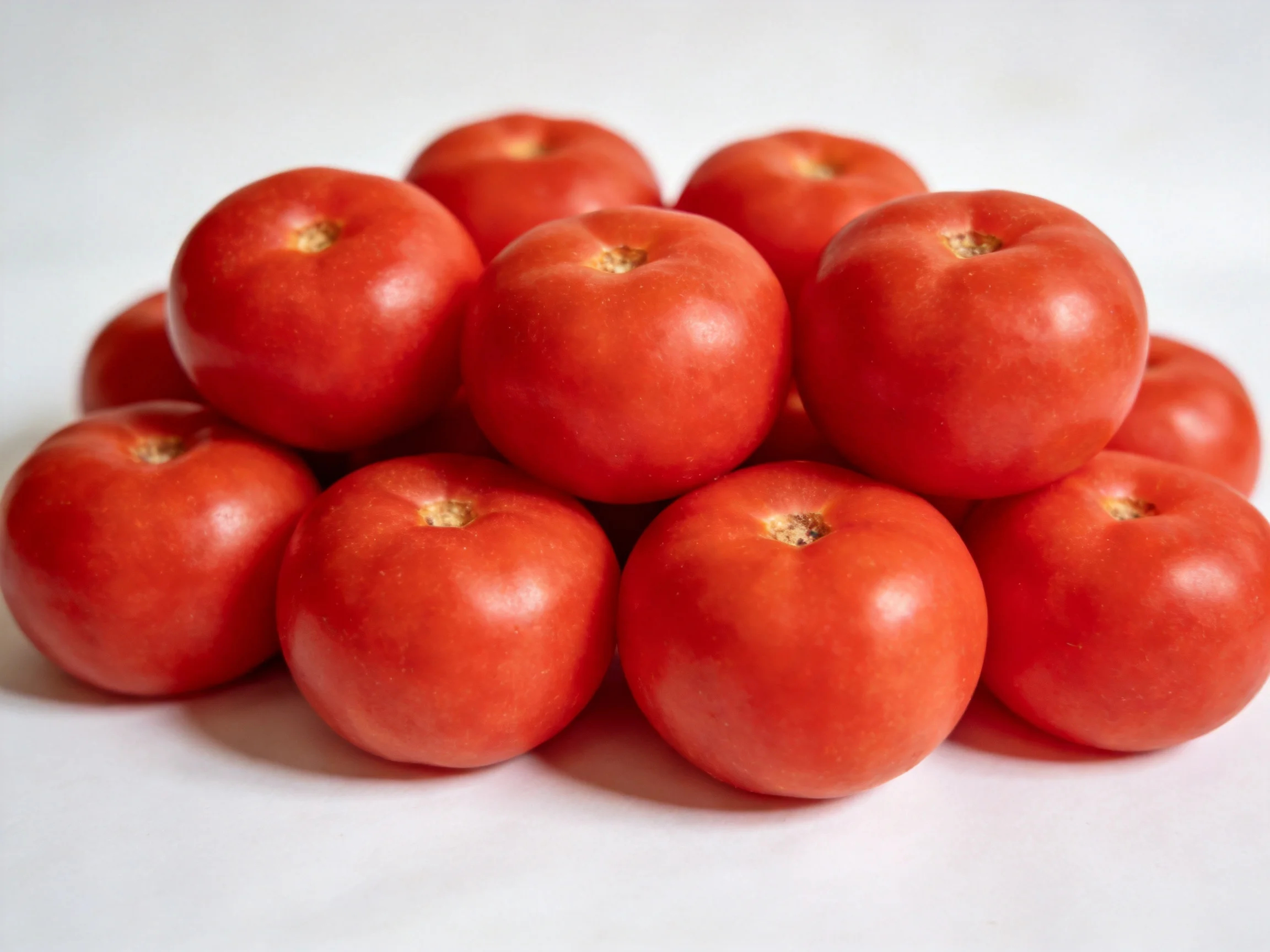 A pile of twelve vibrant red tomatoes arranged in a pyramid