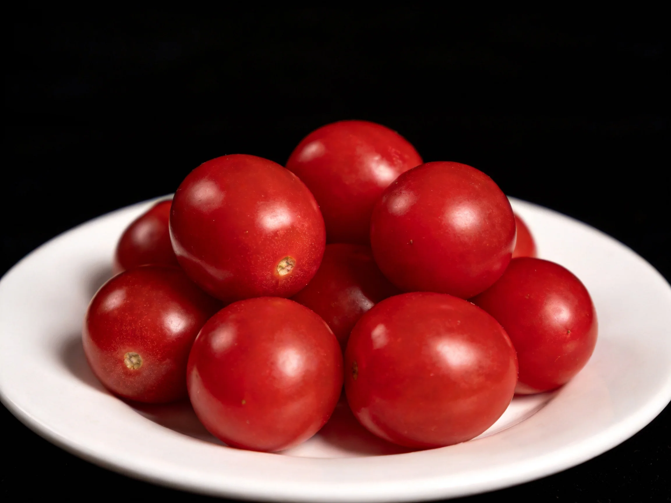 A pile of vibrant red cherry tomatoes arranged on a white plate