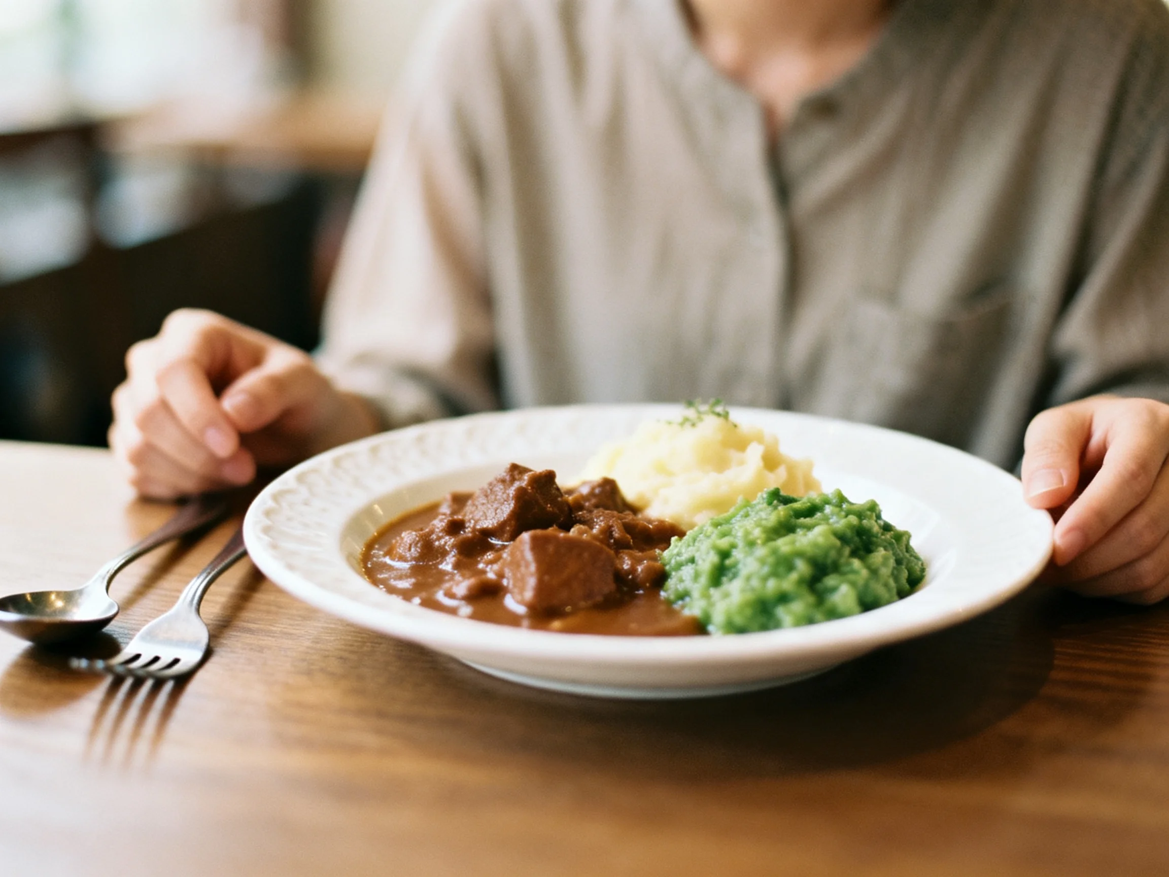 A plate of beef stew, mashed potatoes, and green peas on a wooden table