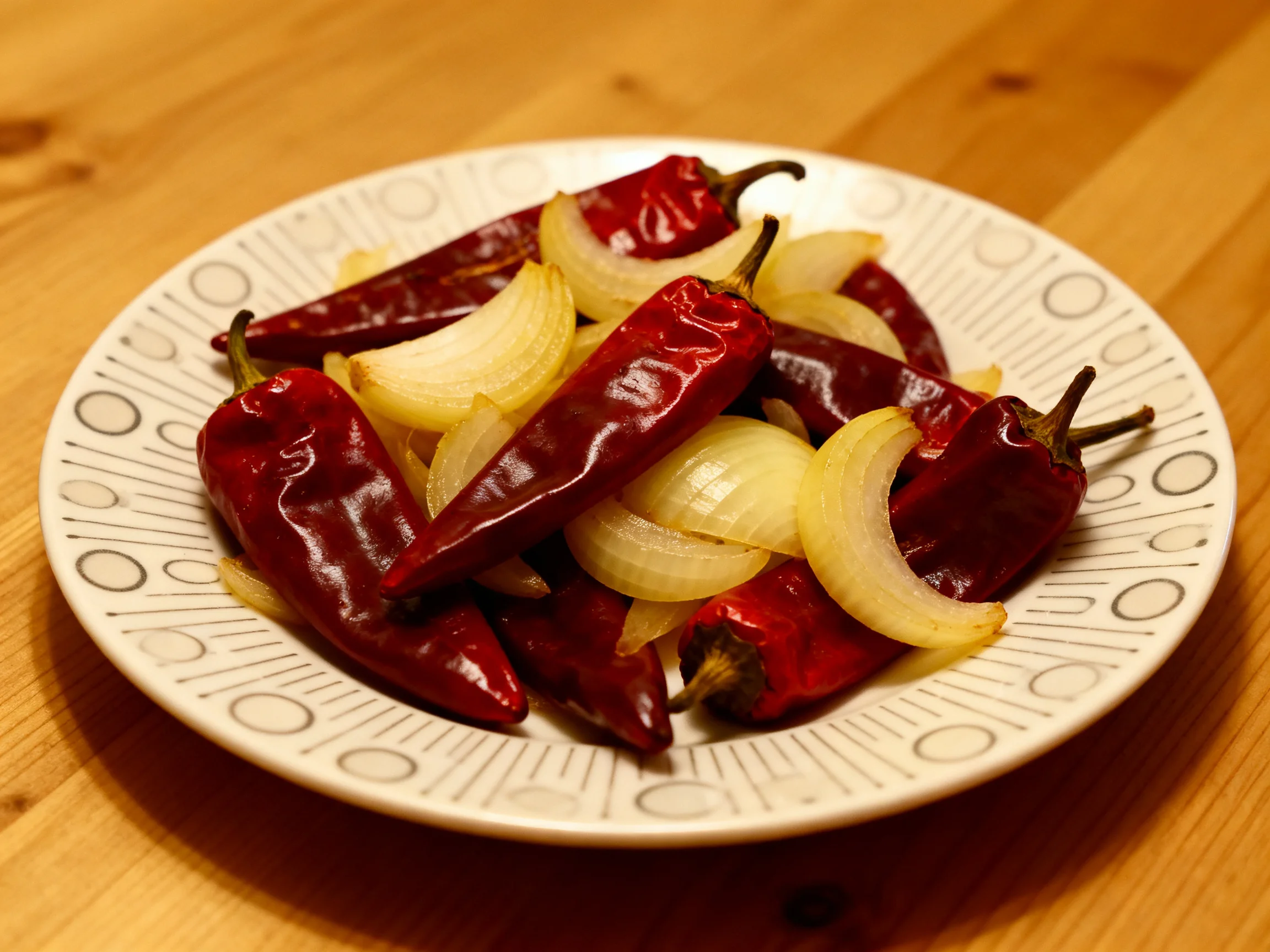 A plate of dried red chilies and sliced onions on a wooden table