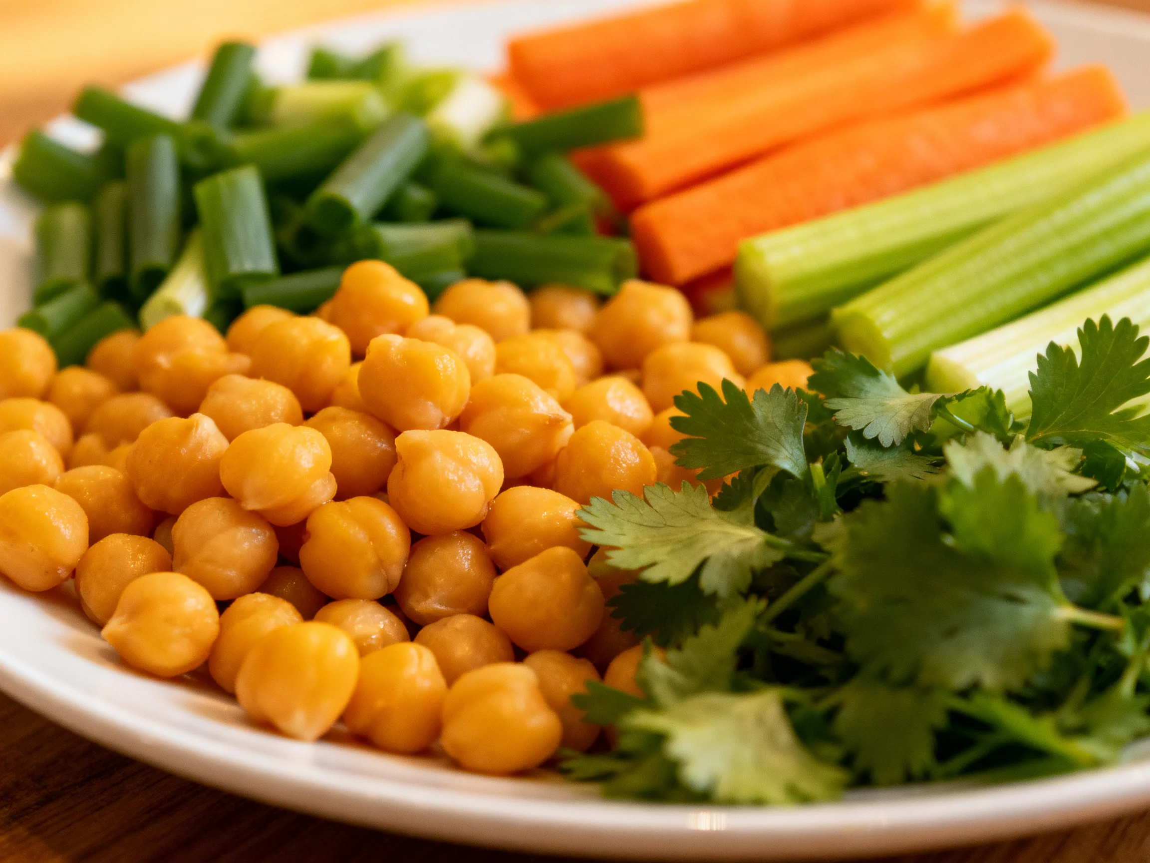 A plate with cooked chickpeas, carrot sticks, celery, scallions, and fresh cilantro