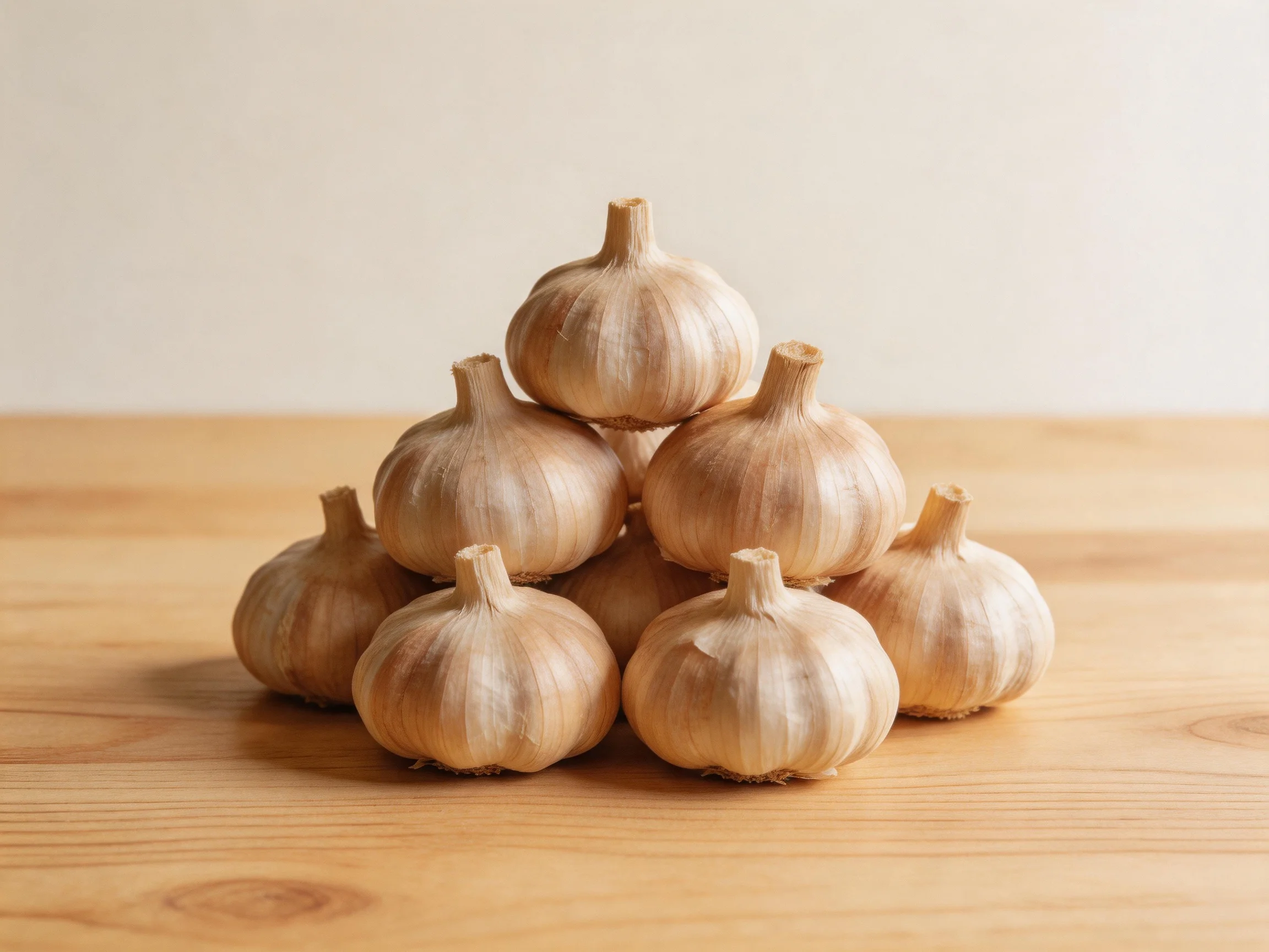 A pyramid of ten light brown garlic bulbs on a wooden surface