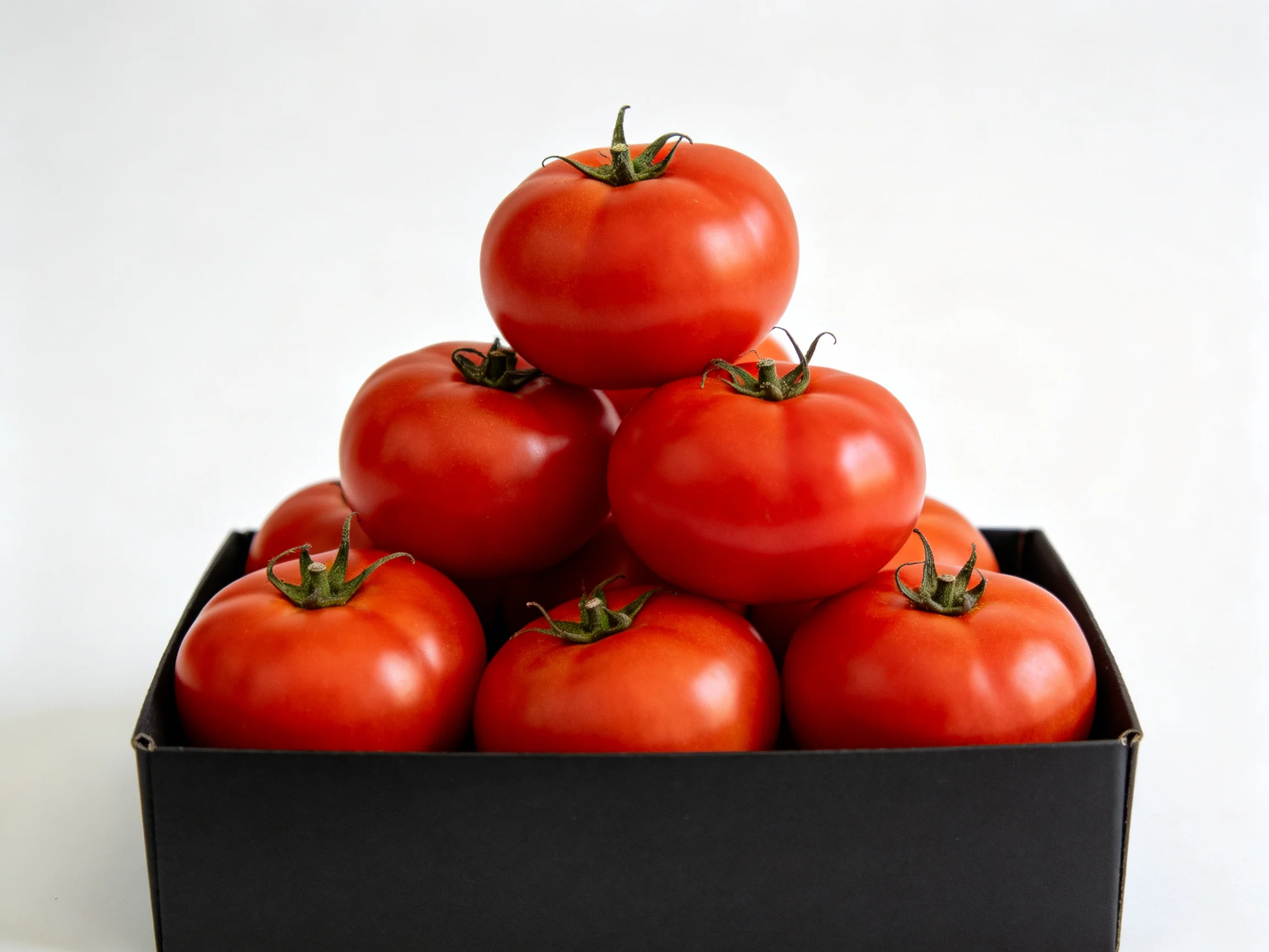 A pyramid of vibrant red tomatoes stacked in a black rectangular container
