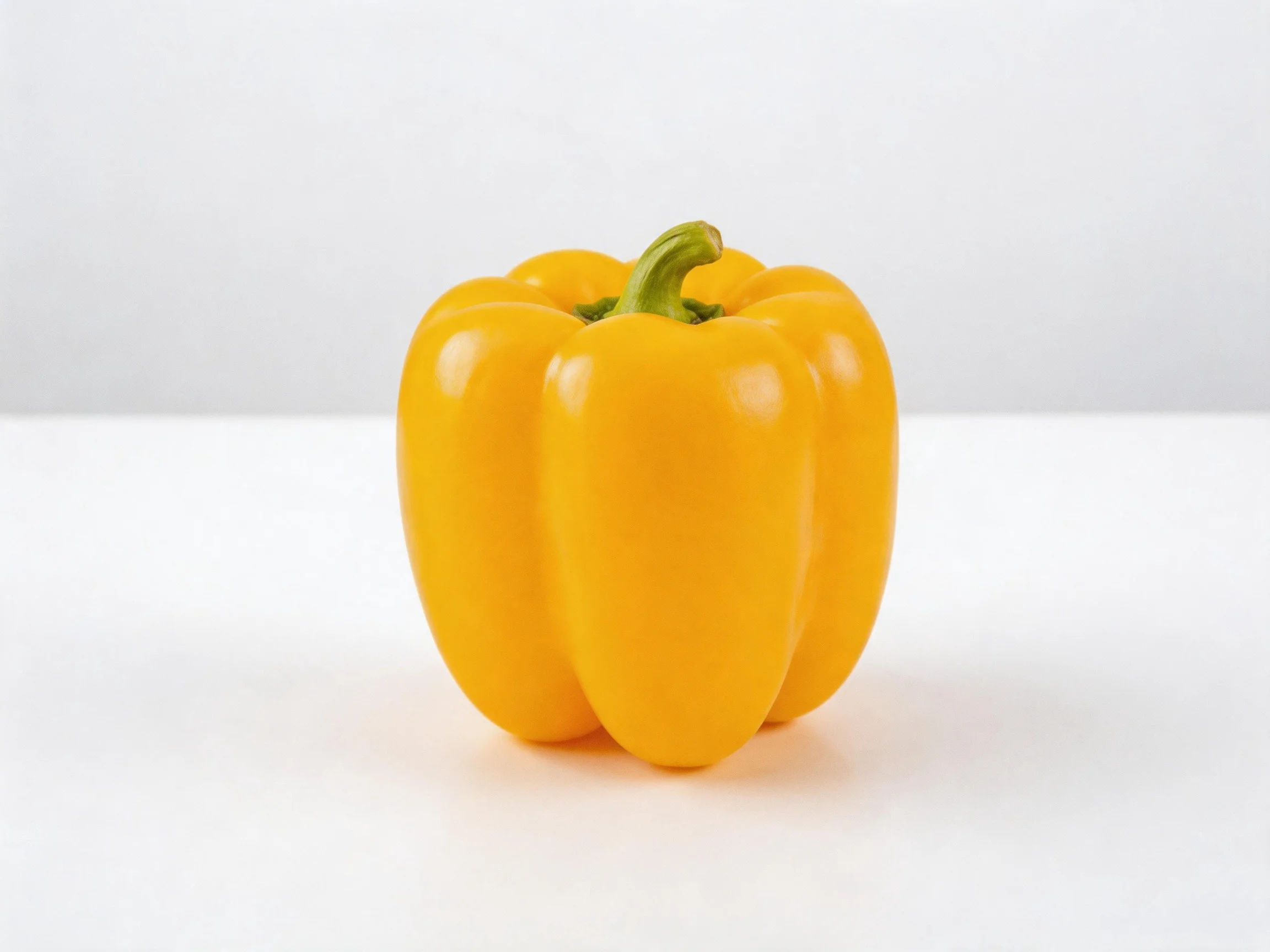A single bright yellow bell pepper centered on a plain white surface