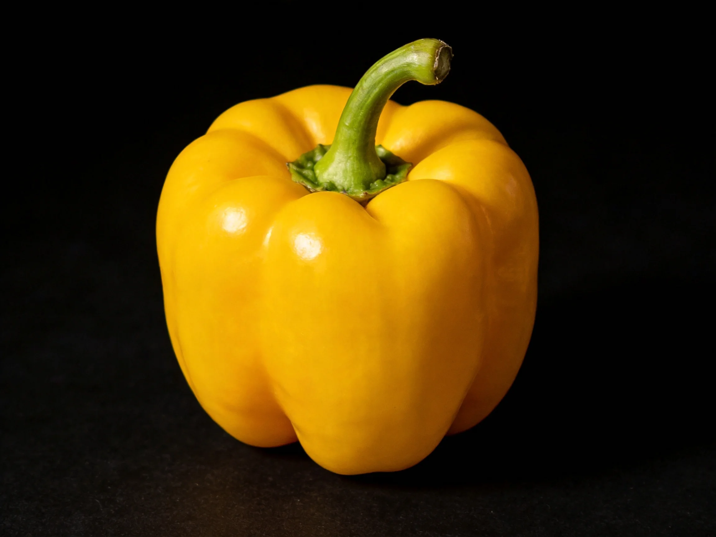 A single vibrant yellow bell pepper centered on a black background